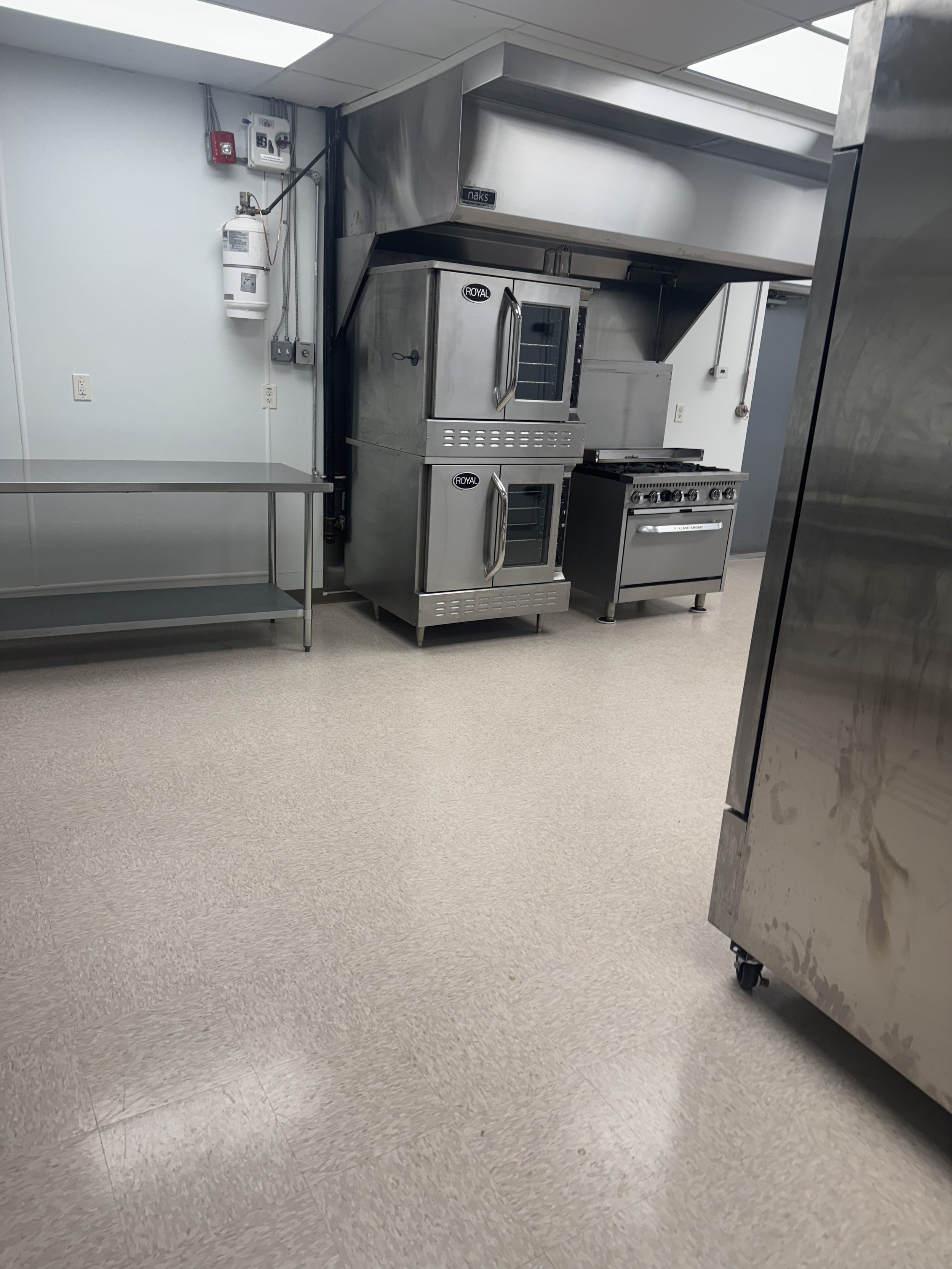 Commercial kitchen with stainless steel appliances, including a double oven, stove, and storage shelves.