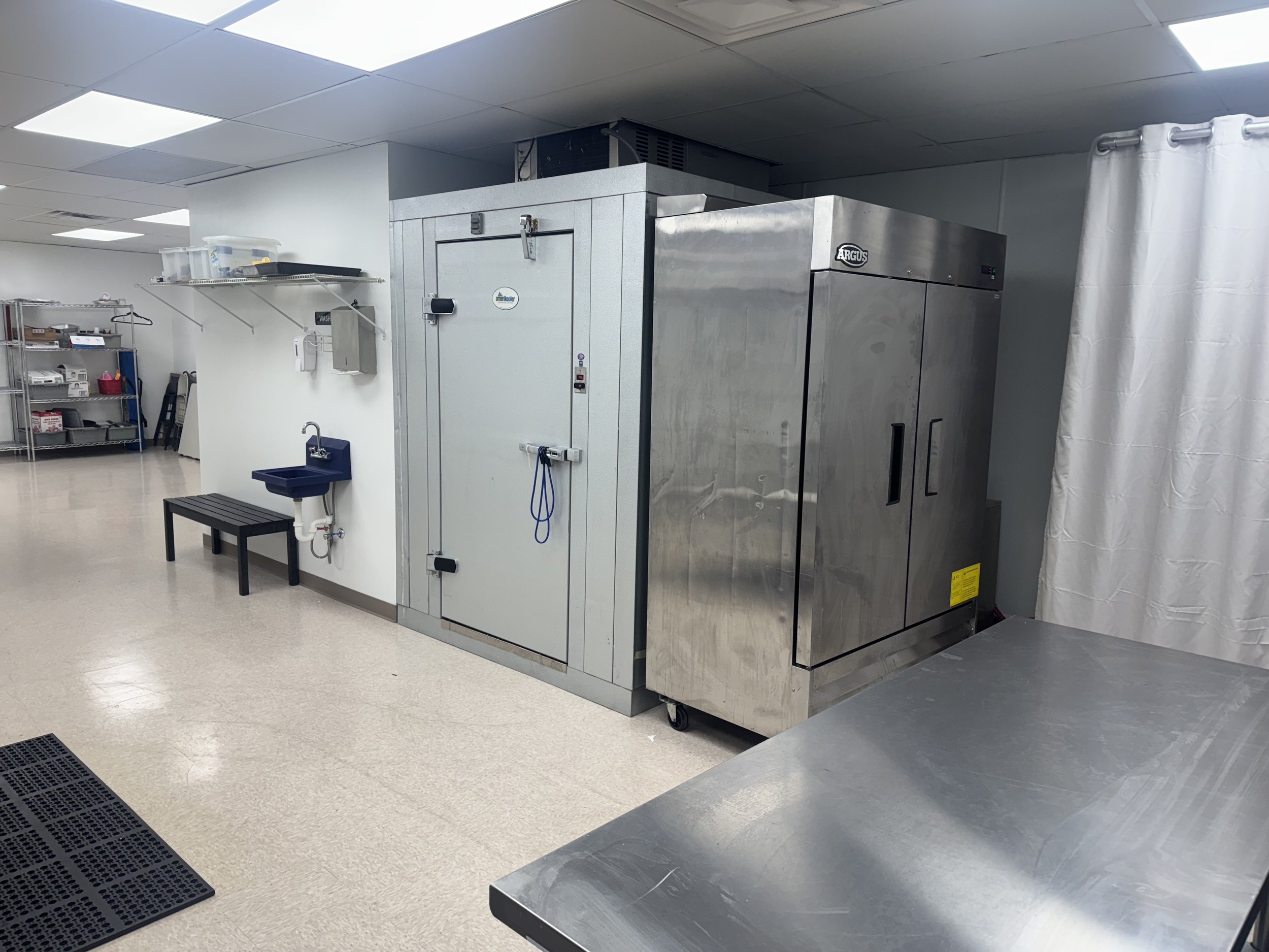 Sterile commercial kitchen or laboratory with stainless steel equipment, a small sink, and storage shelves.