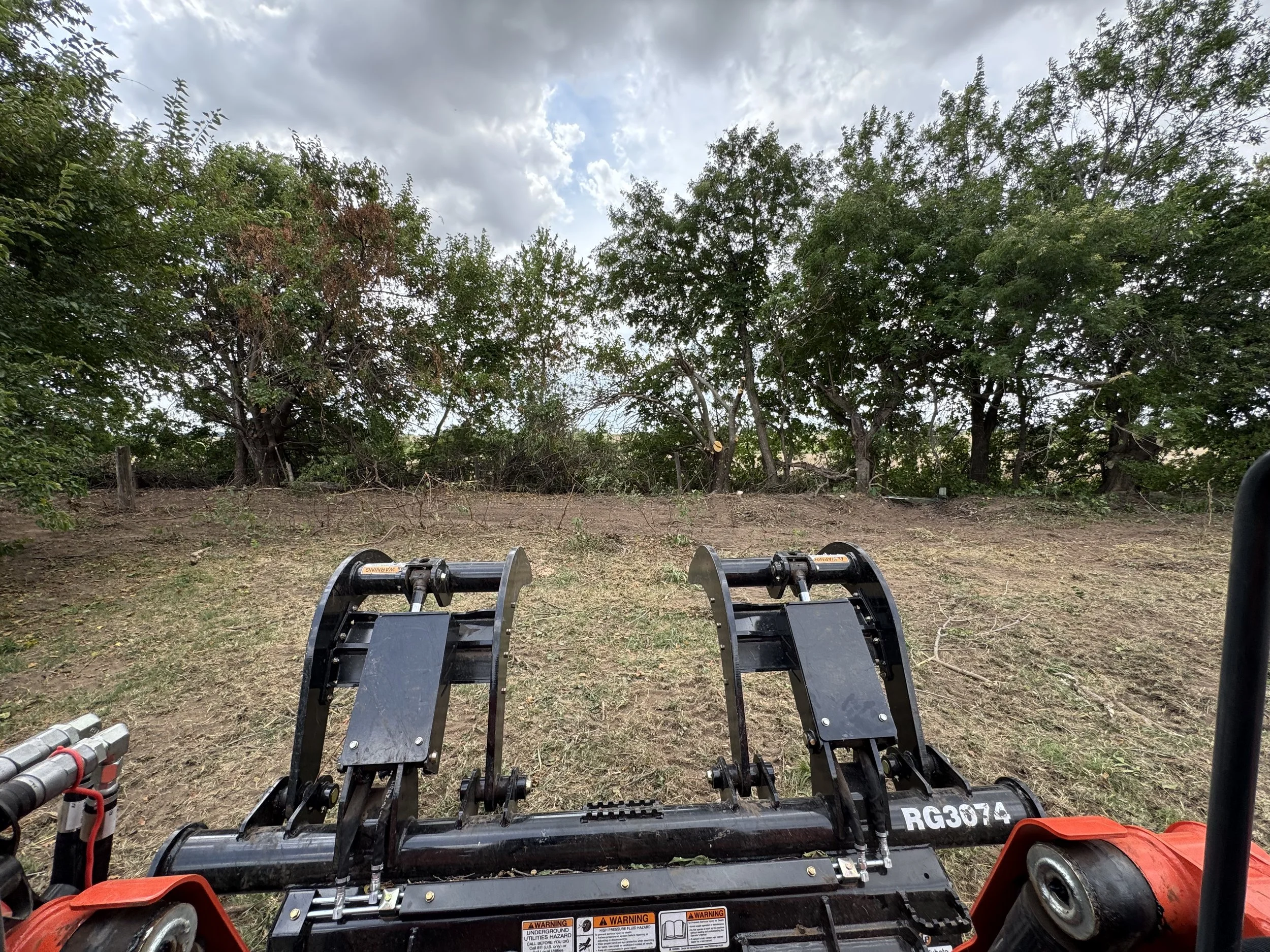 View of a landscape with a dirt clearing and trees in the background, with a piece of heavy machinery in the foreground.