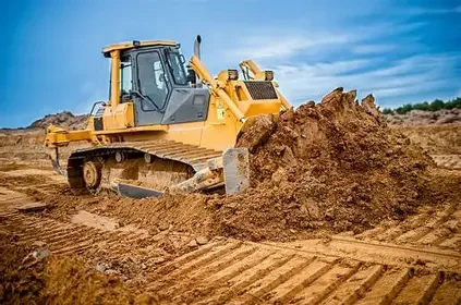 A yellow bulldozer pushing dirt on a construction site under a cloudy blue sky.