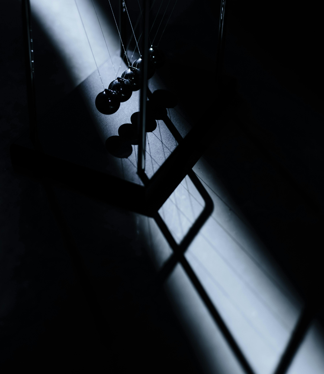 Close-up of a Newton's cradle with black balls, dimly lit with a shadowy background.