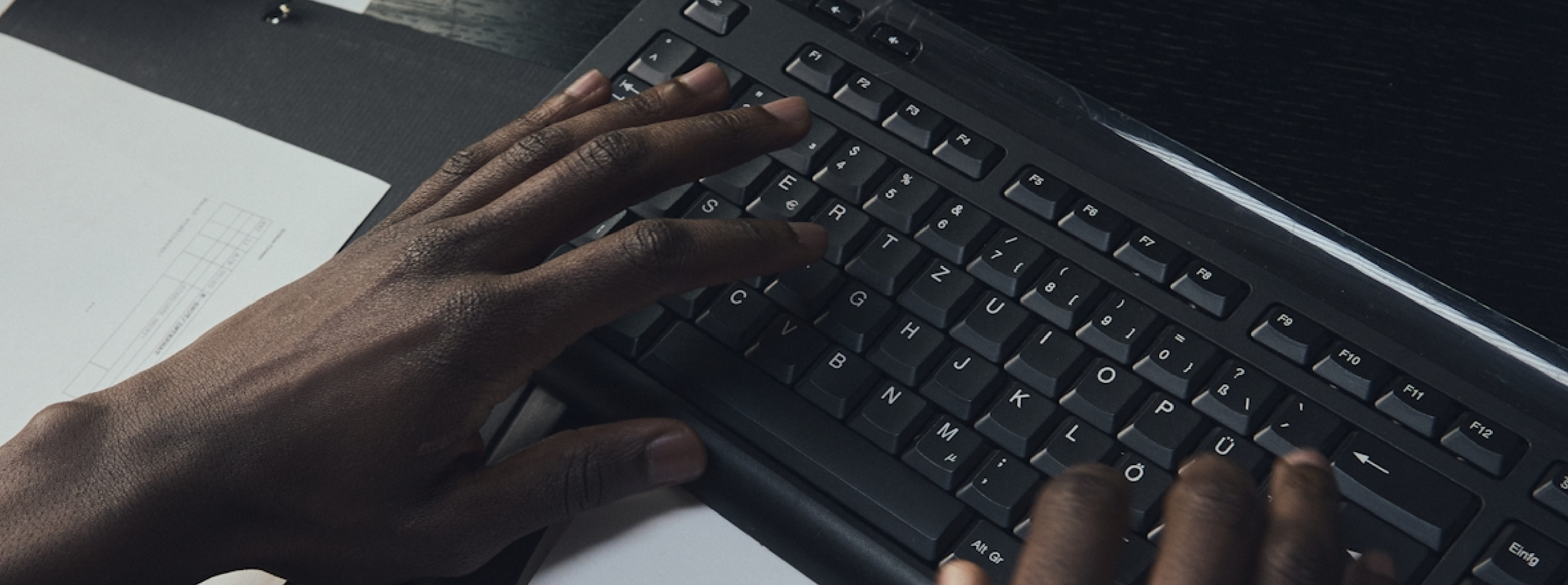 A person's hands type on a black computer keyboard on a desk.