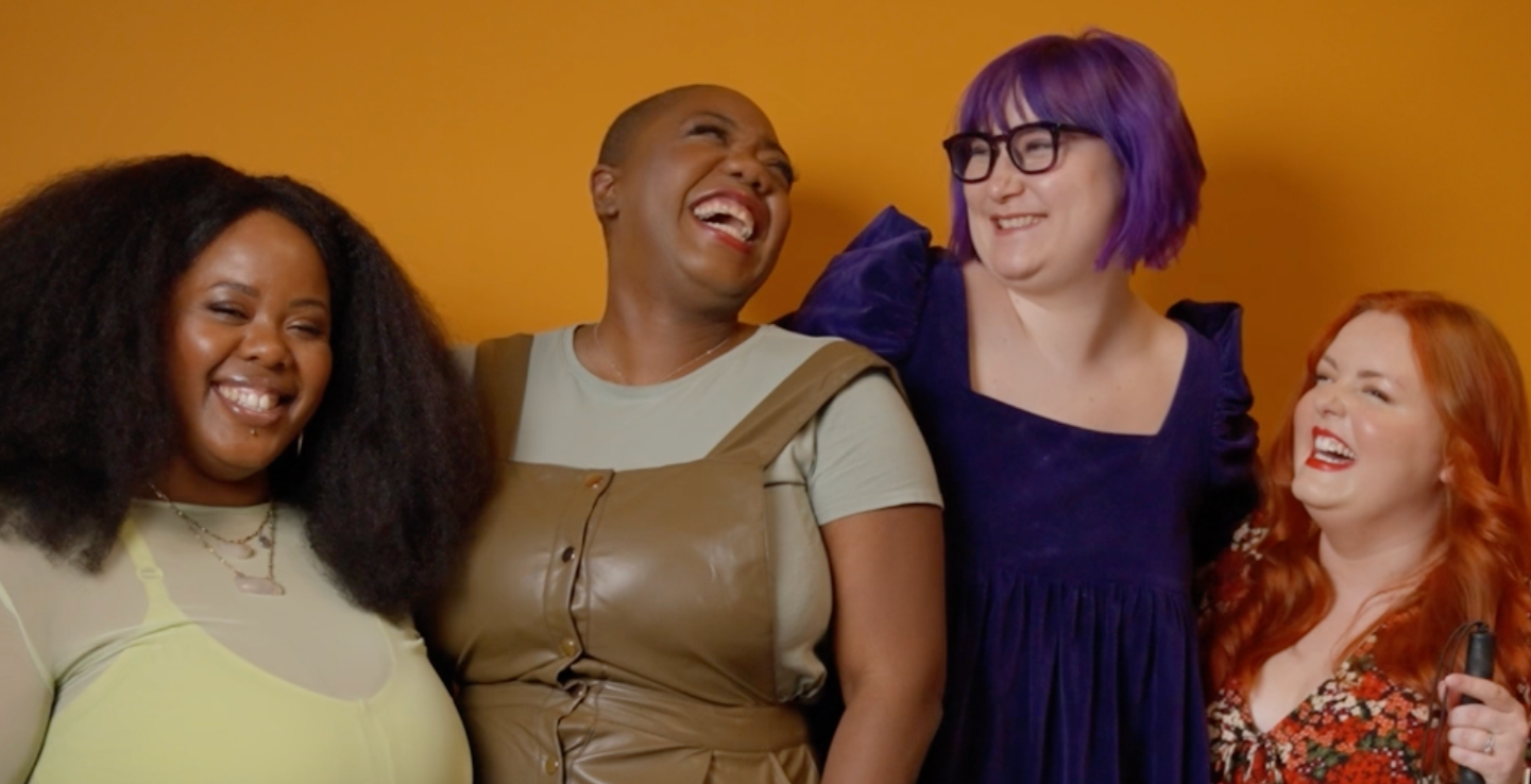 Four women laughing together against a yellow background.