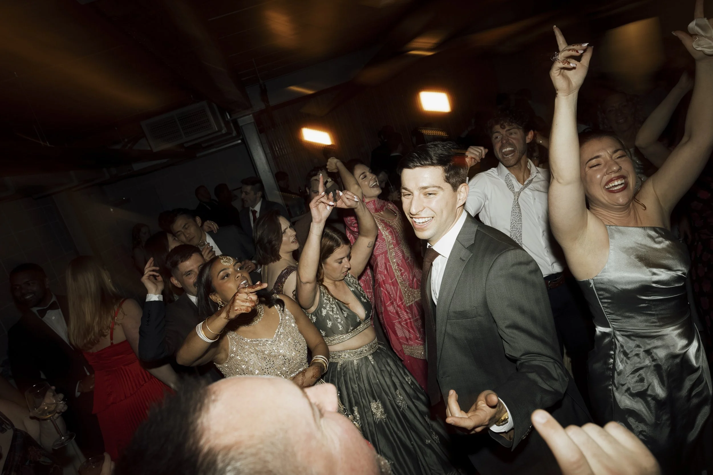 People dancing and celebrating at an upstate NY wedding, with a man in a suit and several women in colorful dresses dancing joyfully.