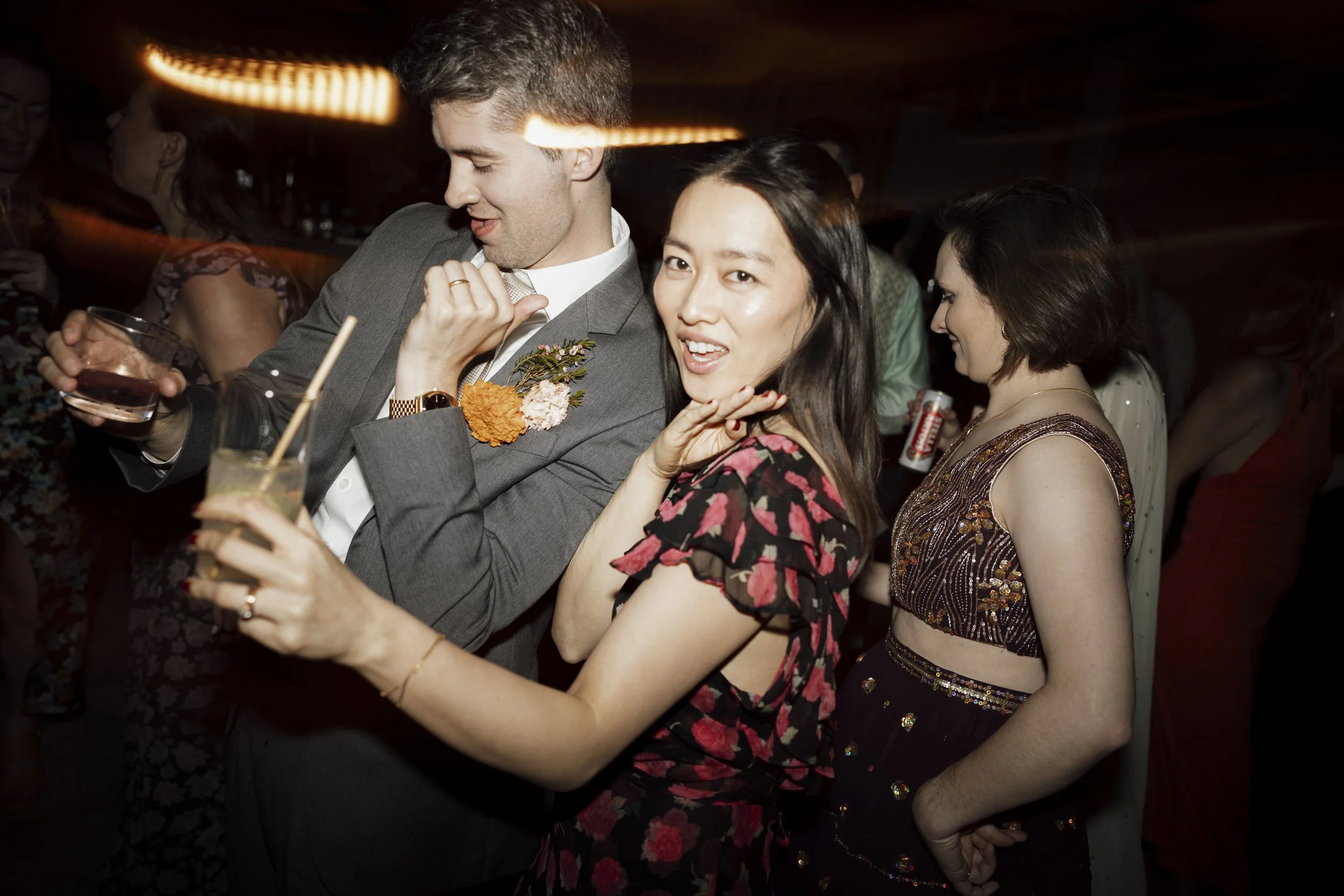 Group of young adults dancing and having fun at an upstate NY wedding holding drinks in a dark, festive environment.
