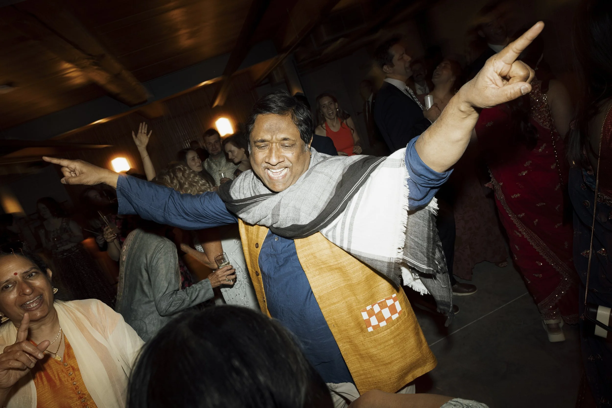 A man dancing and singing with his eyes closed and arms outstretched at an upstate NY wedding, surrounded by other guests dancing in the background.