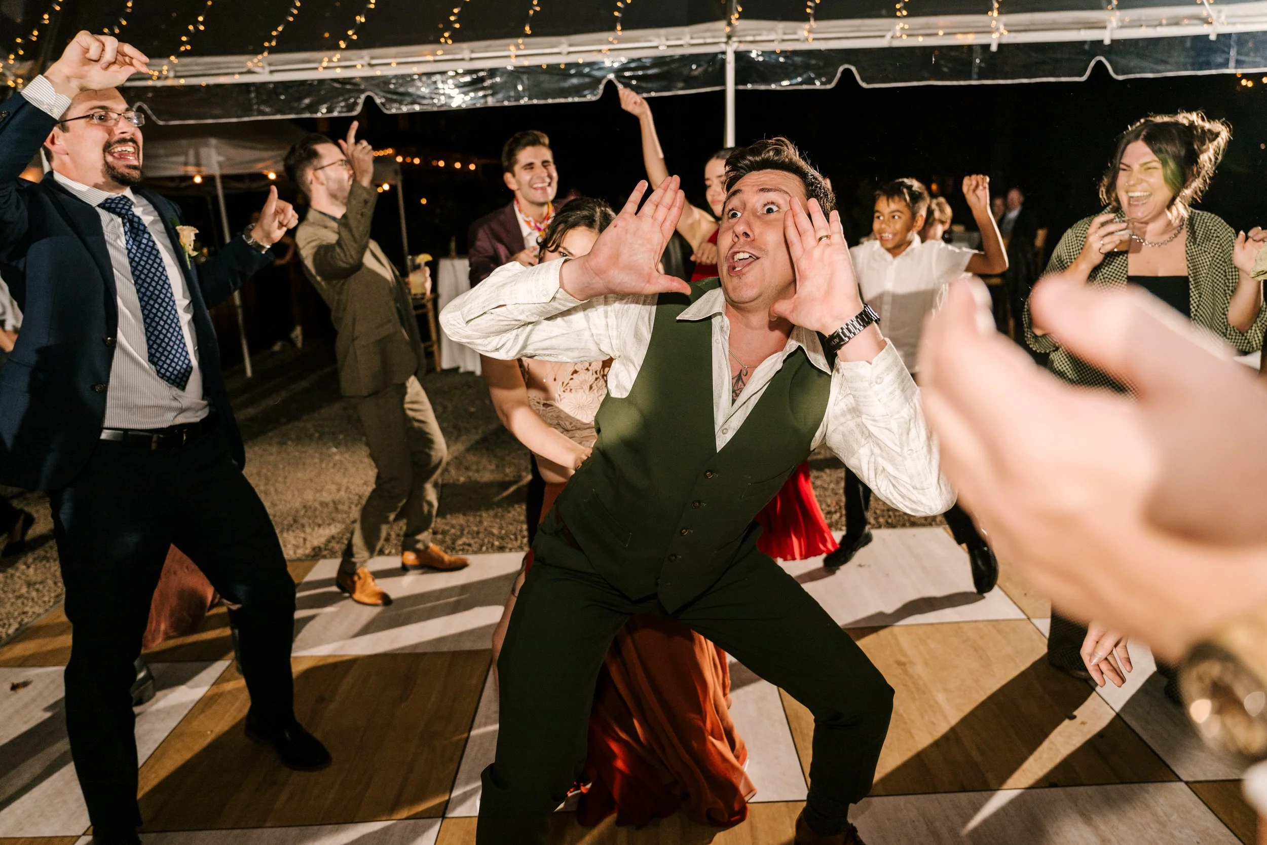 People dancing and having fun at an upstate NY wedding reception under a tent with string lights at night.