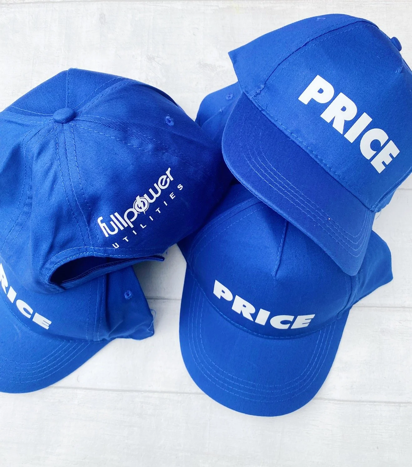 Three blue baseball caps with white text, one says 'PRICÉ' and the others say 'fullpower OUTLiTERS'.