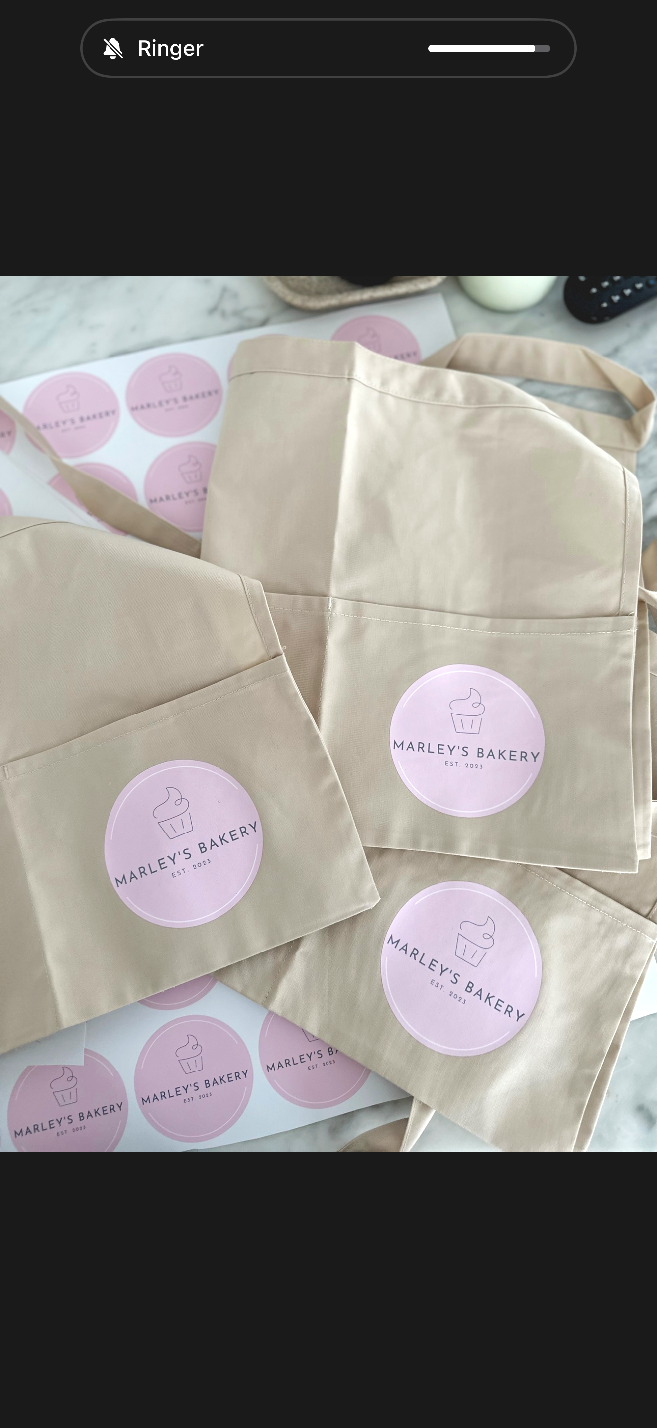 Multiple beige tote bags with round pink stickers that read 'Marley's Bakery EST. 2023' with a cupcake icon, placed on a countertop.