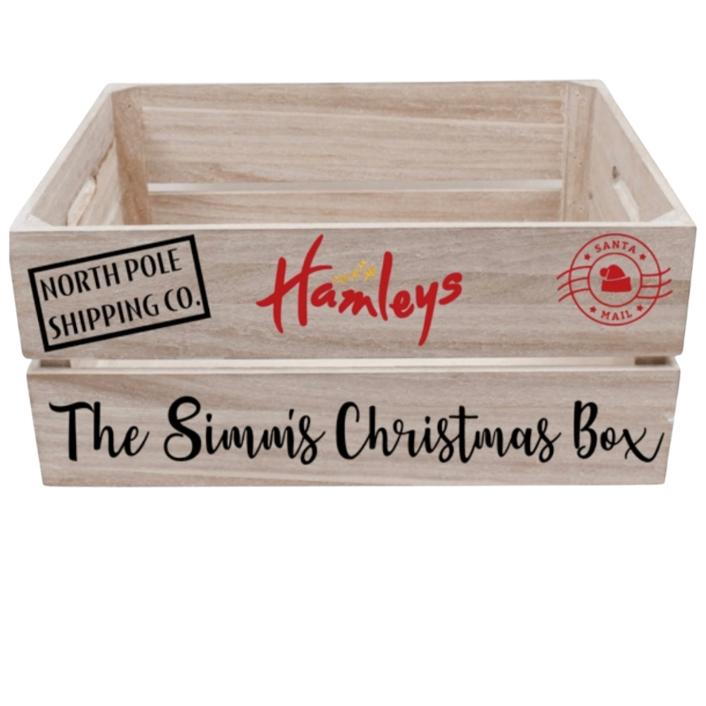 A wooden Christmas box with festive labels including 'North Pole Shipping Co.' and 'Santa Mail,' featuring the logo 'Hamleys' and the text 'The Simi's Christmas Box'.