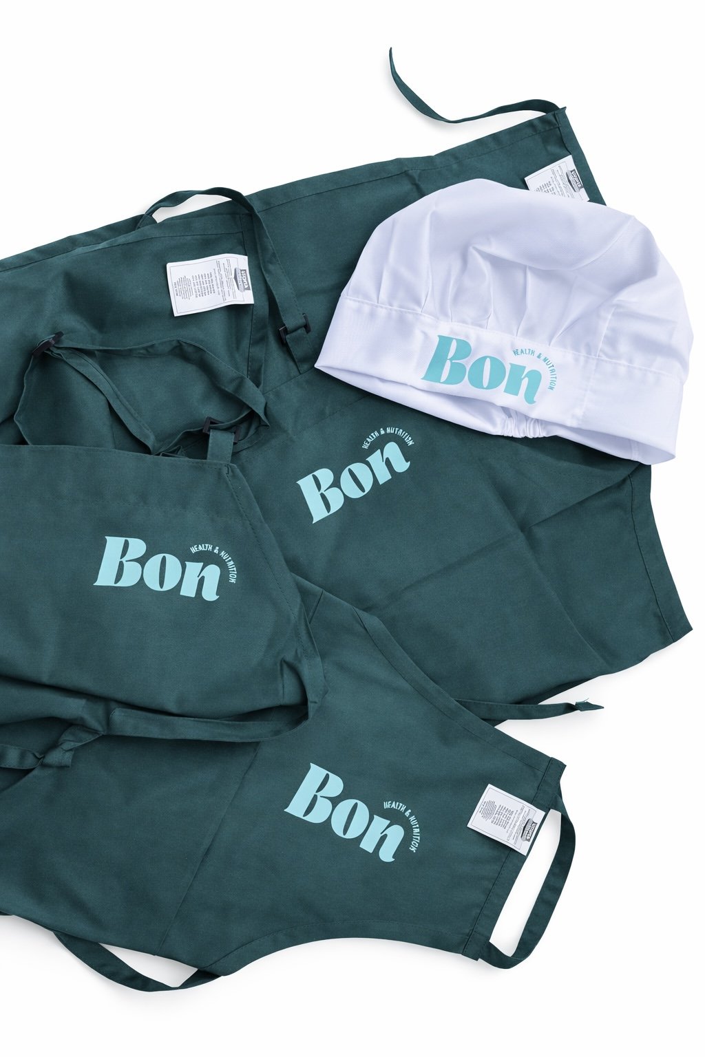 Collection of green aprons and a white chef's hat with the words 'Bon' printed on them, all themed around health and nutrition.