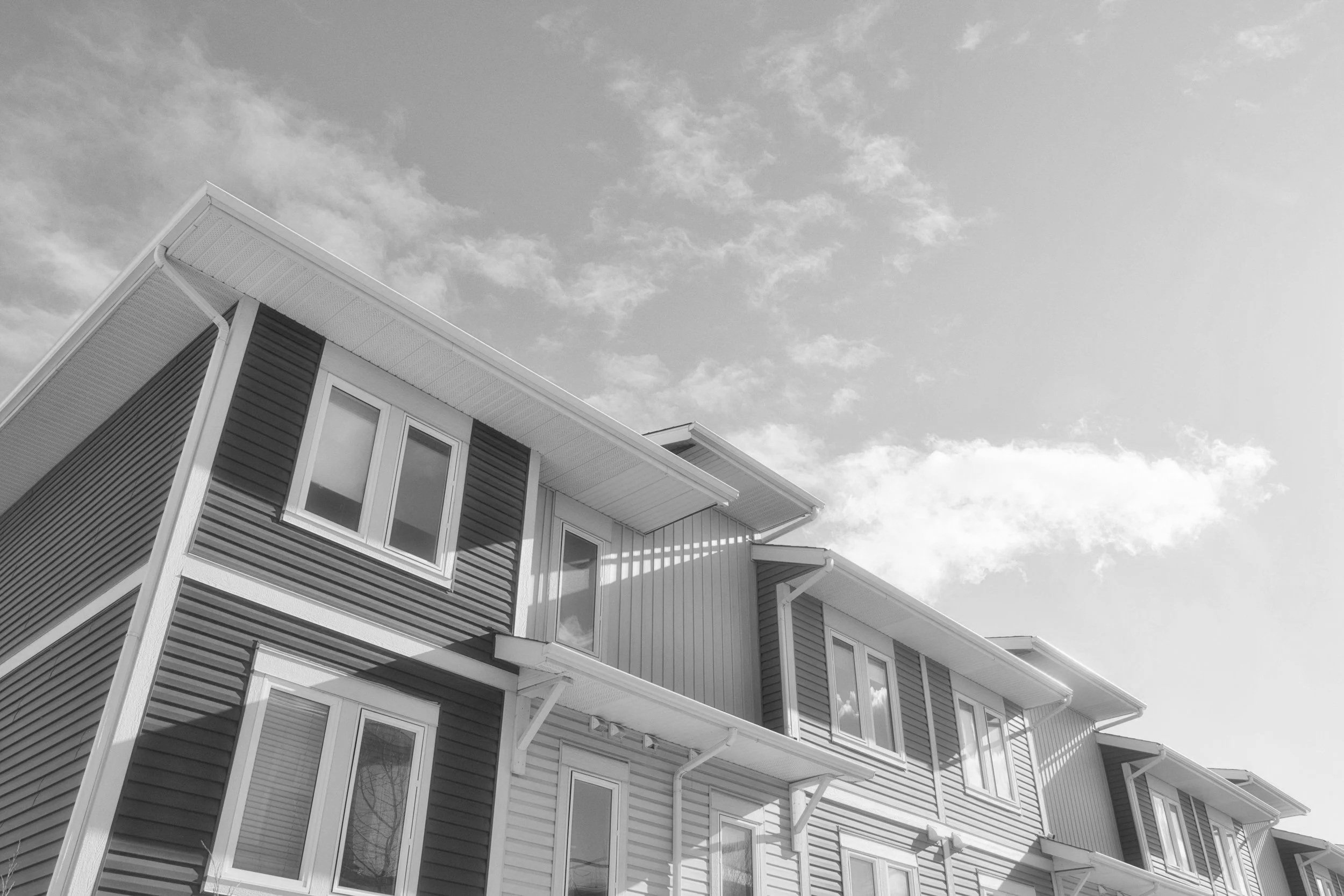 A modern multi-story residential building with horizontal siding and multiple windows, under a partly cloudy sky.