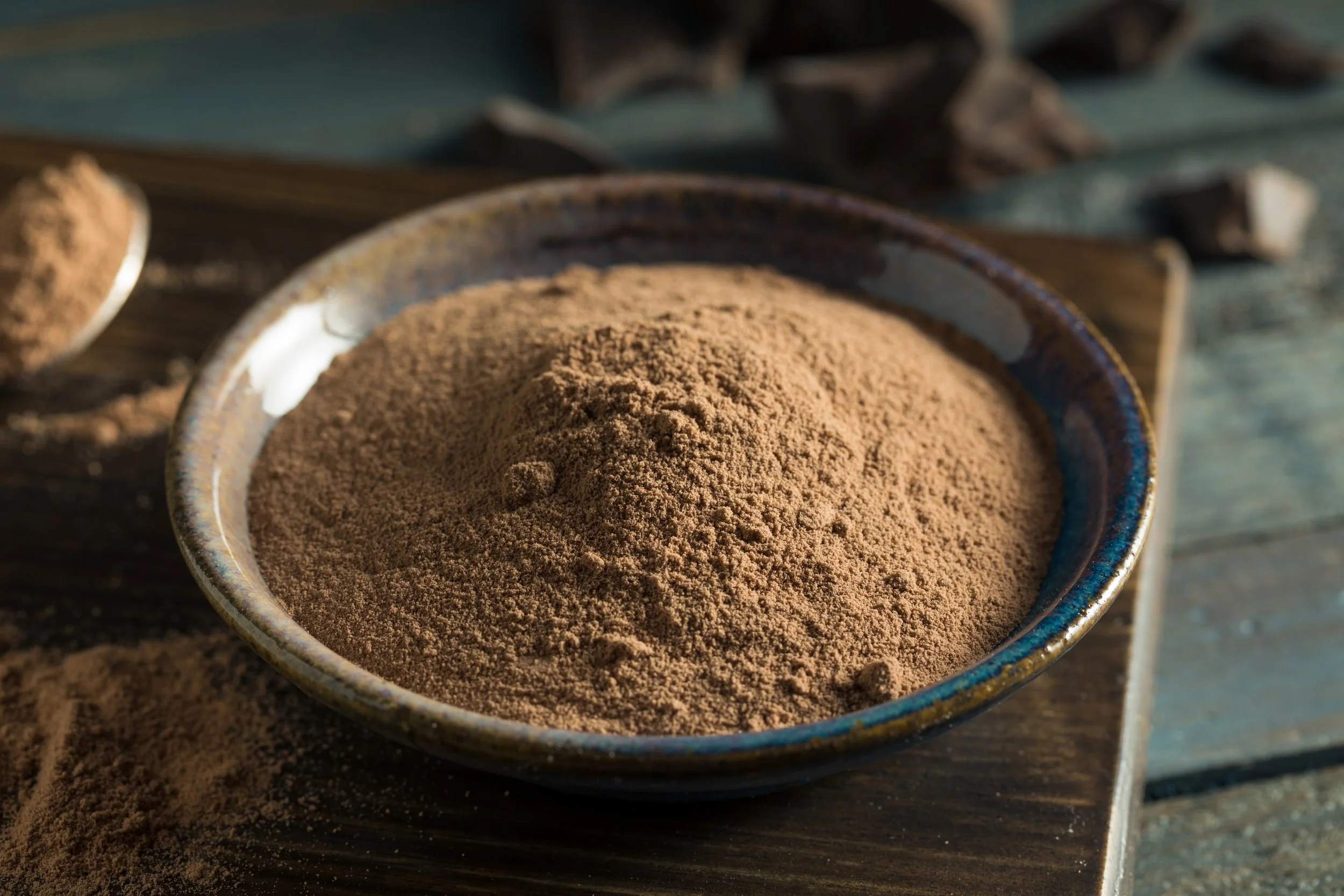 Close-up of a ceramic bowl filled with cocoa powder on a rustic wooden surface.