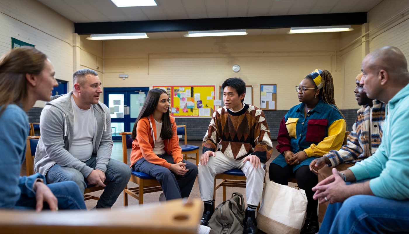 A group of people sitting in a circle in a classroom or community room, engaged in conversation.