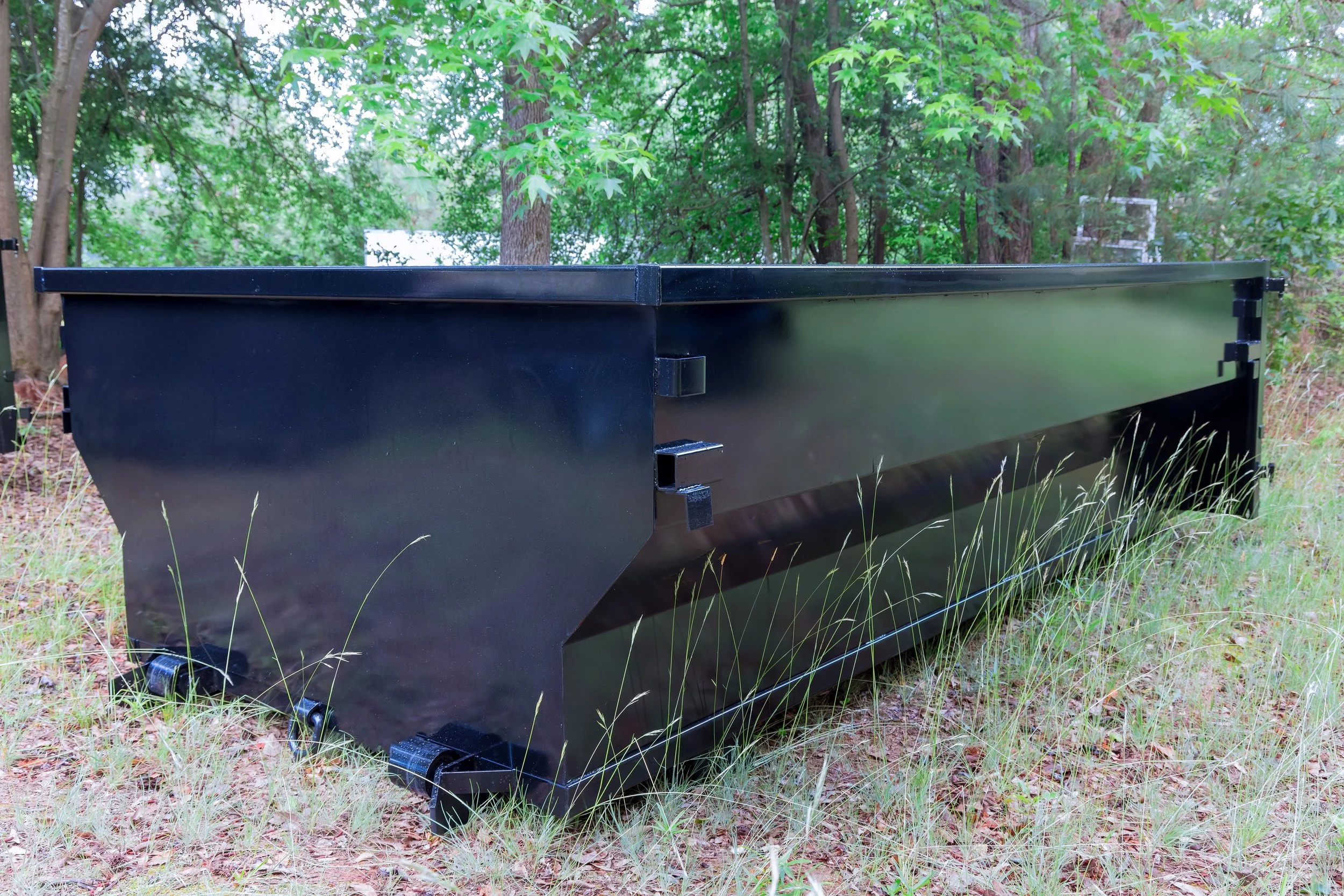 Large black metal outdoor storage container on grass in a wooded area.