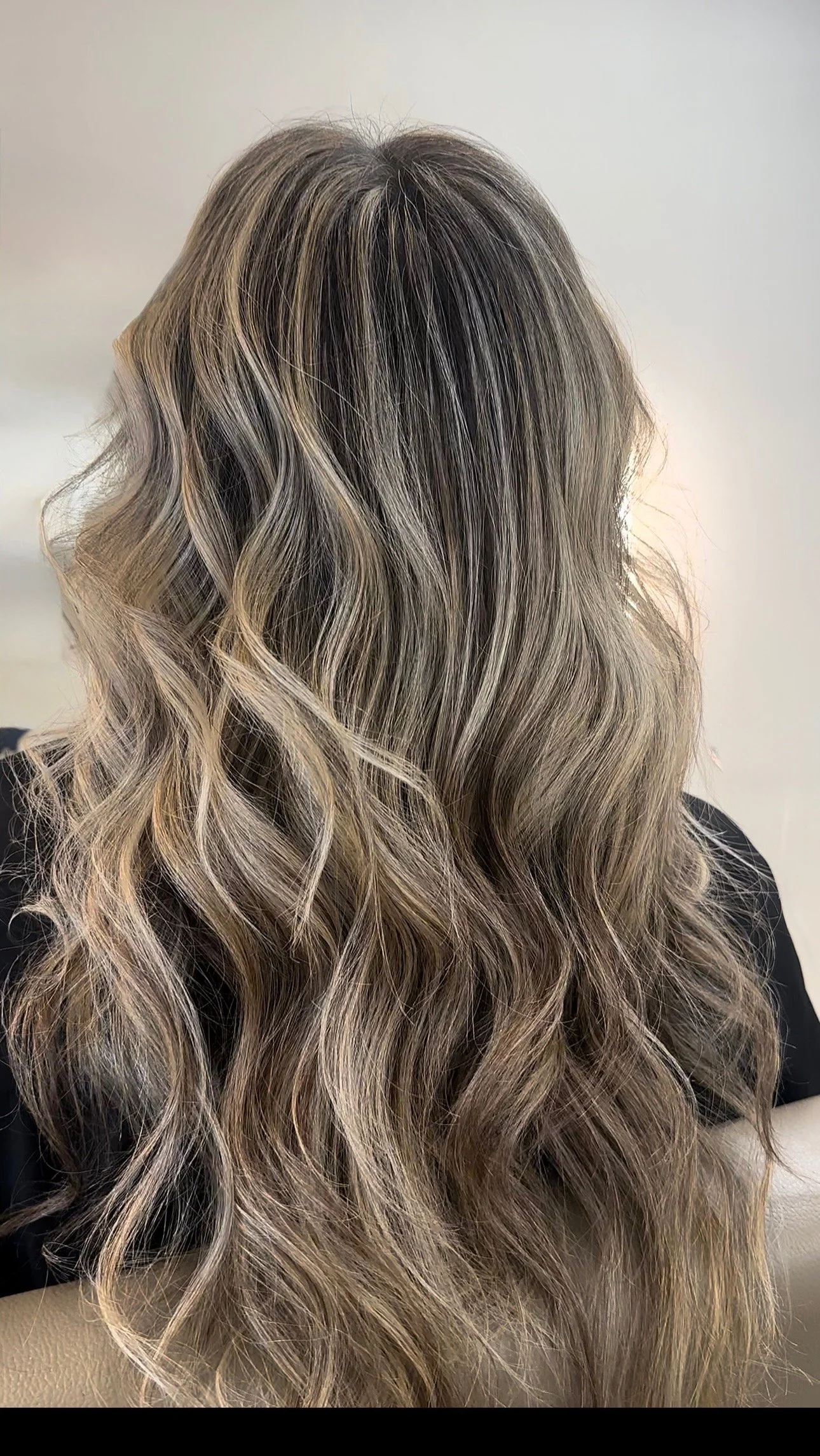Back view of a person with long, wavy, blonde hair with darker roots.