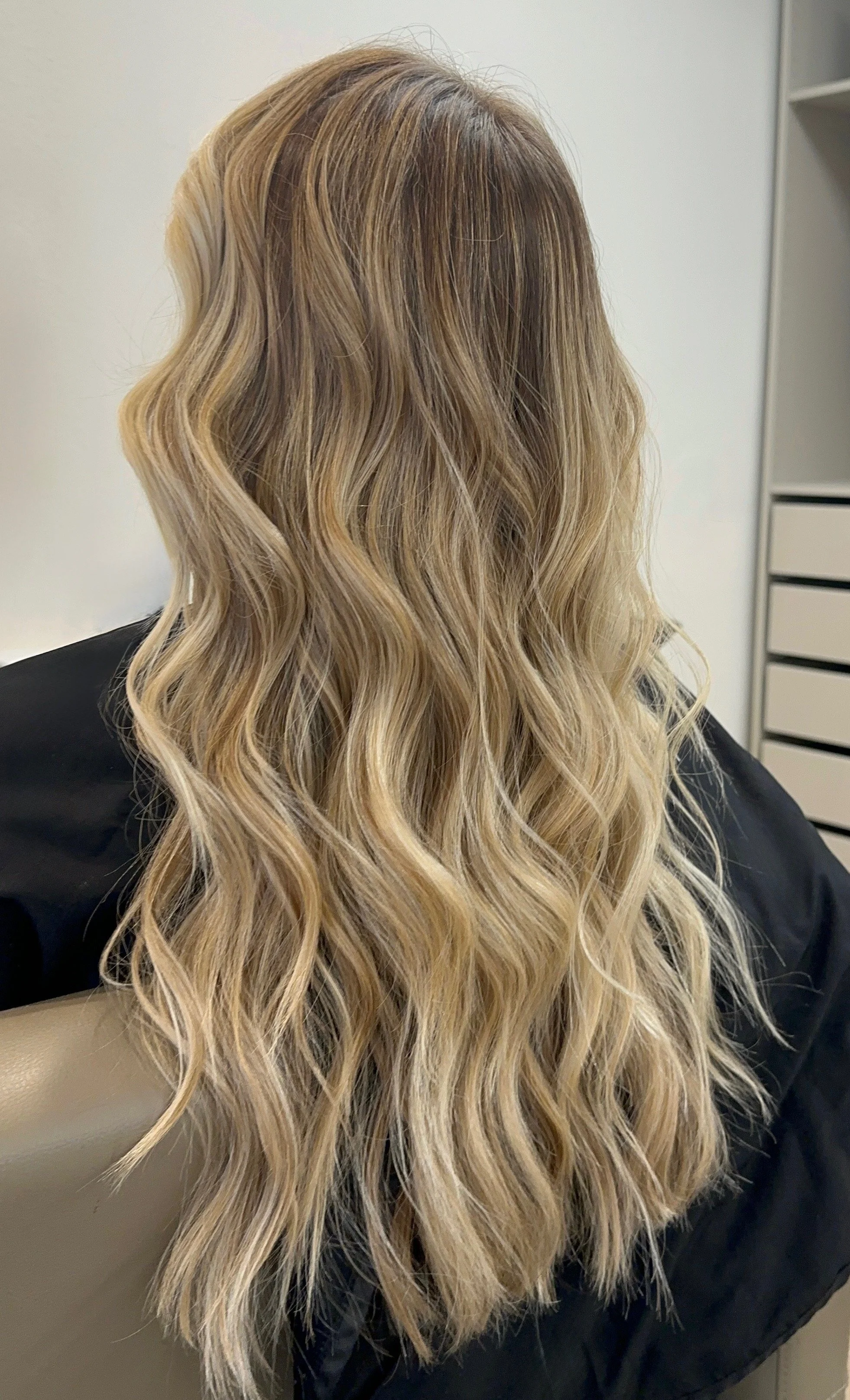 Back of a woman with long, wavy, blonde hair sitting in a salon chair.