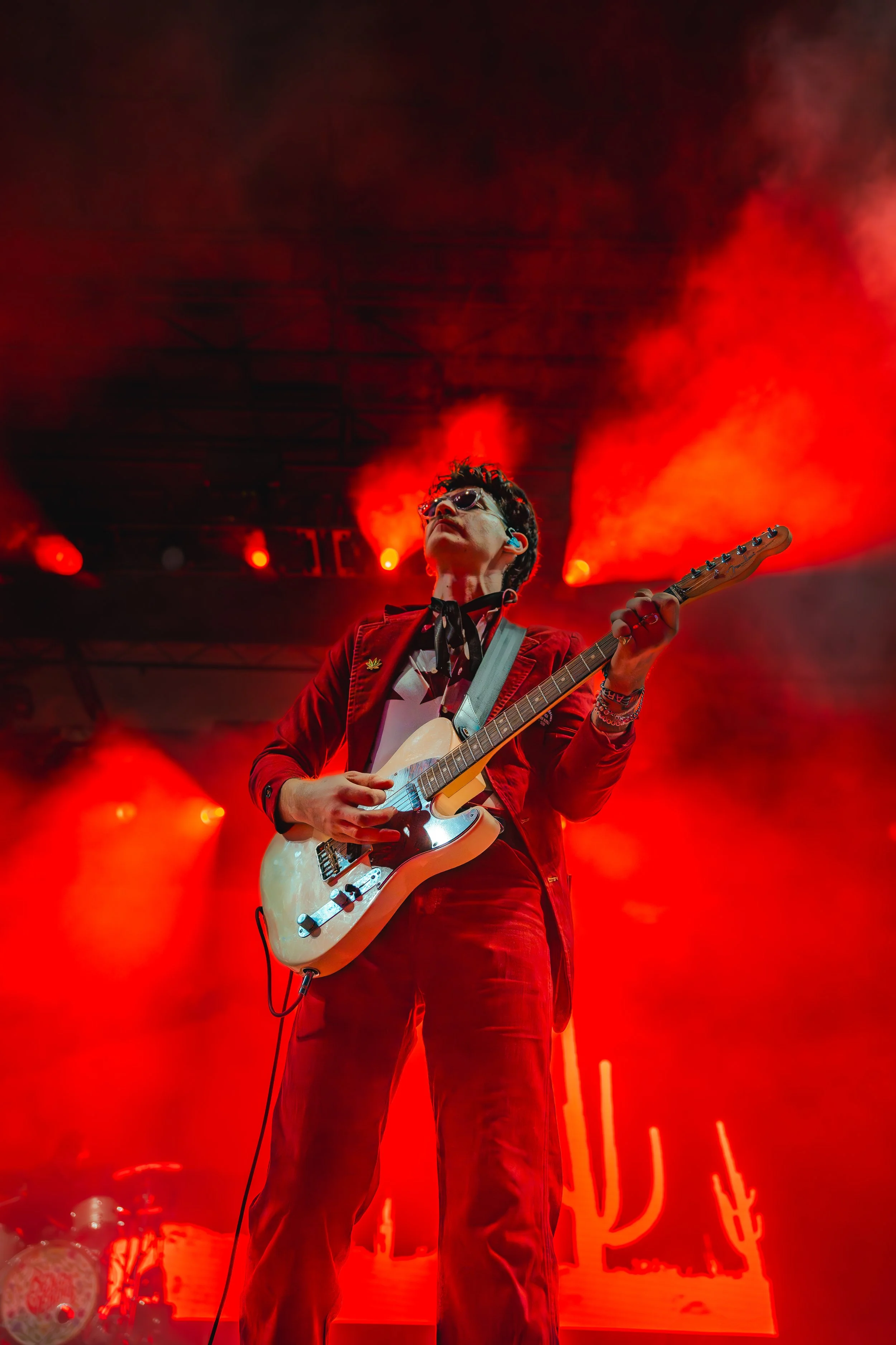 A musician playing an electric guitar on stage with red lighting and fog.