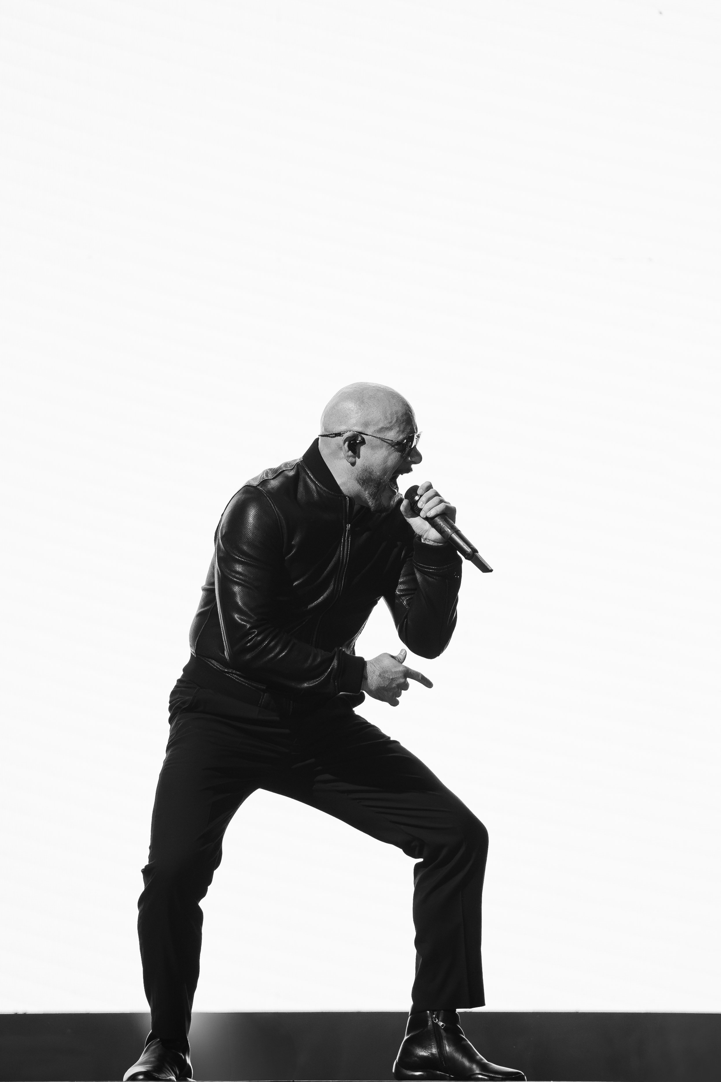 A man in a leather jacket and glasses singing into a microphone on a stage.