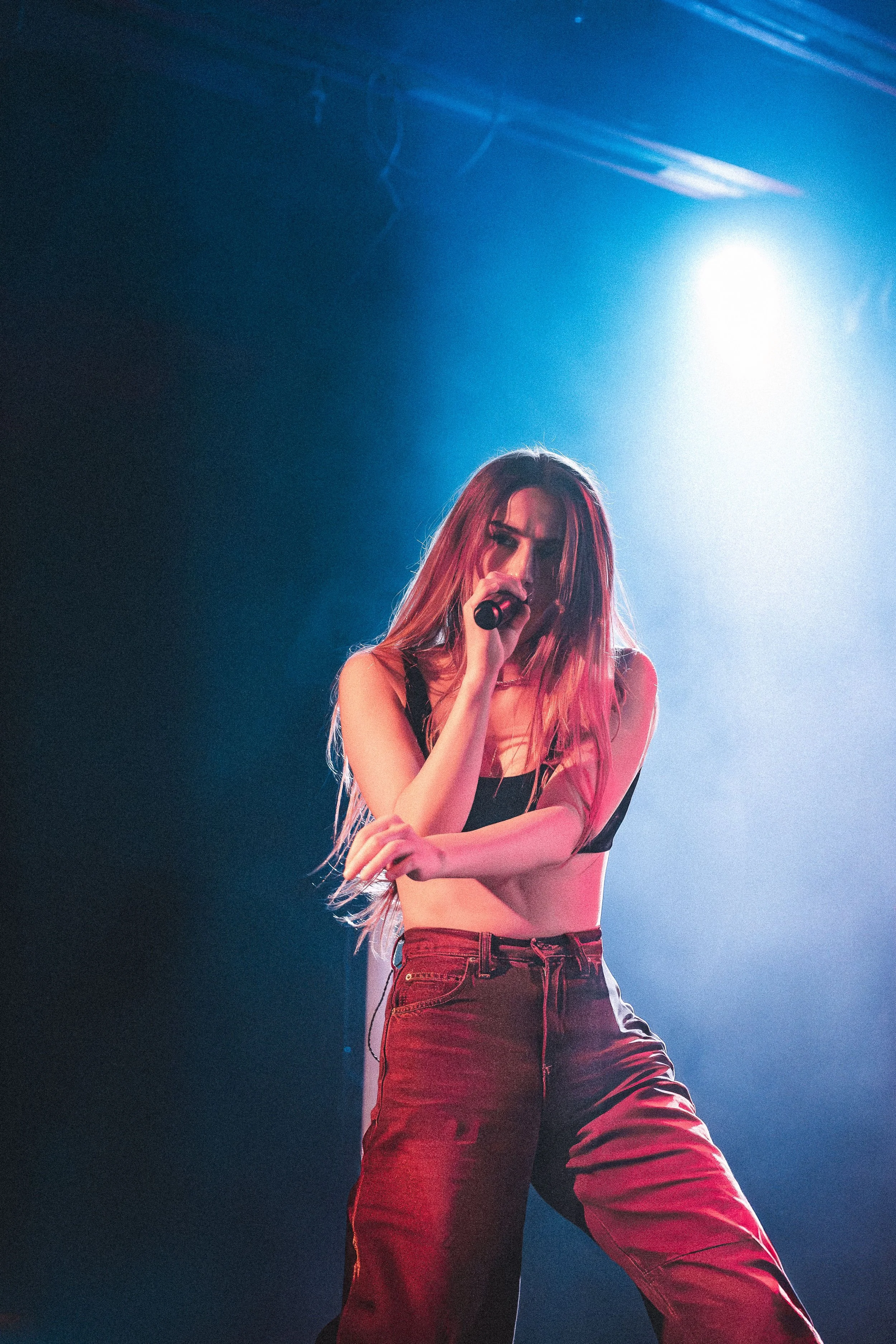 A young woman with long, red hair performing on stage, holding a microphone and singing.