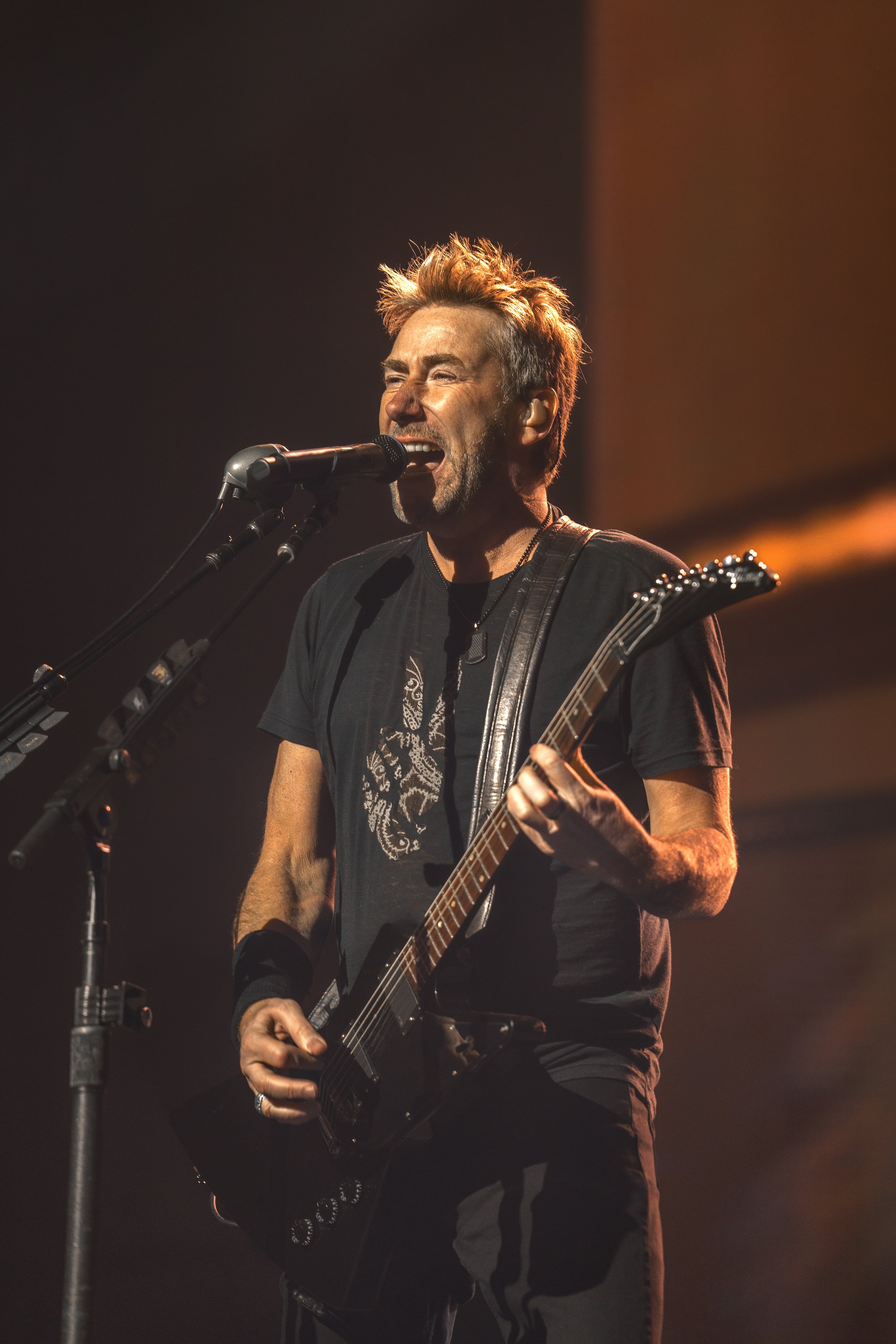 A man singing into a microphone while playing an electric guitar on stage.