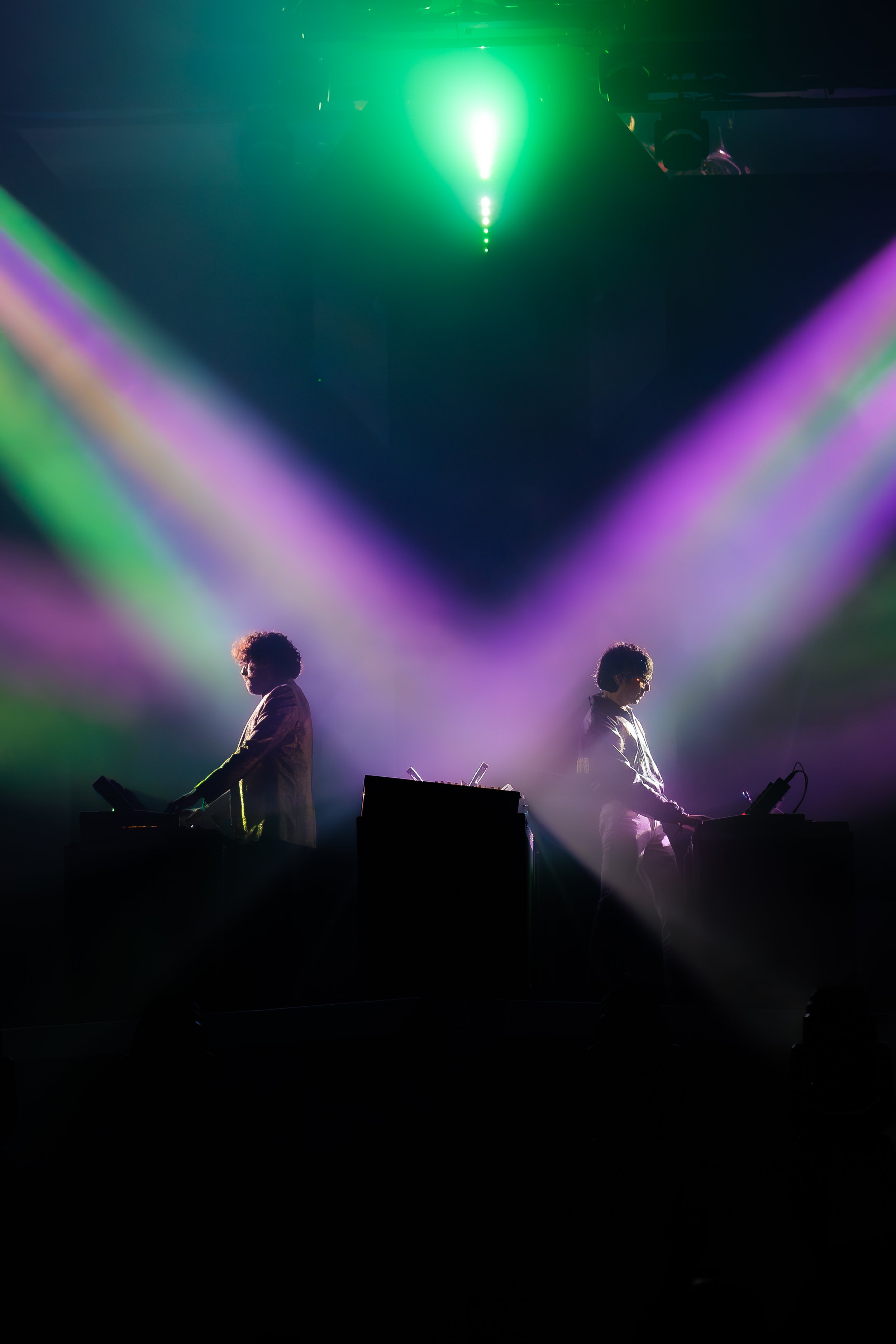 Two performers on stage silhouette with colorful laser lights and fog effects, creating a vibrant concert atmosphere.