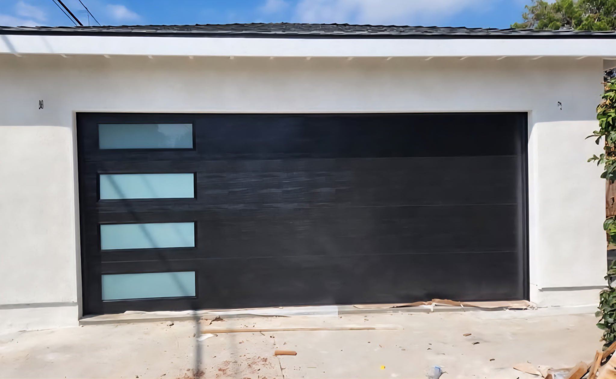 Front view of a modern black garage door with four frosted glass panels on the left side, set in a white wall of a house.