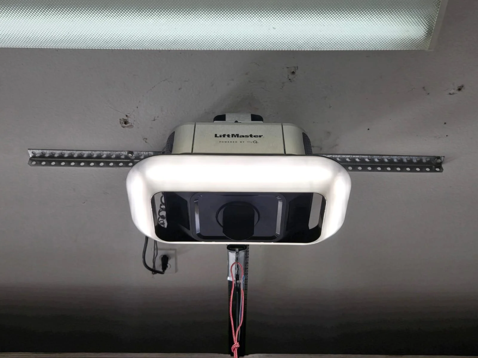 Garage door opener with a white, rounded light frame, installed on a gray ceiling with visible screws and some stains or marks.