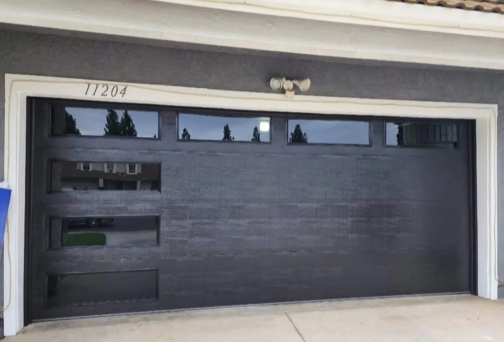 Black garage door with horizontal windows at the top, surrounding white framing, and house number 11204 above it.