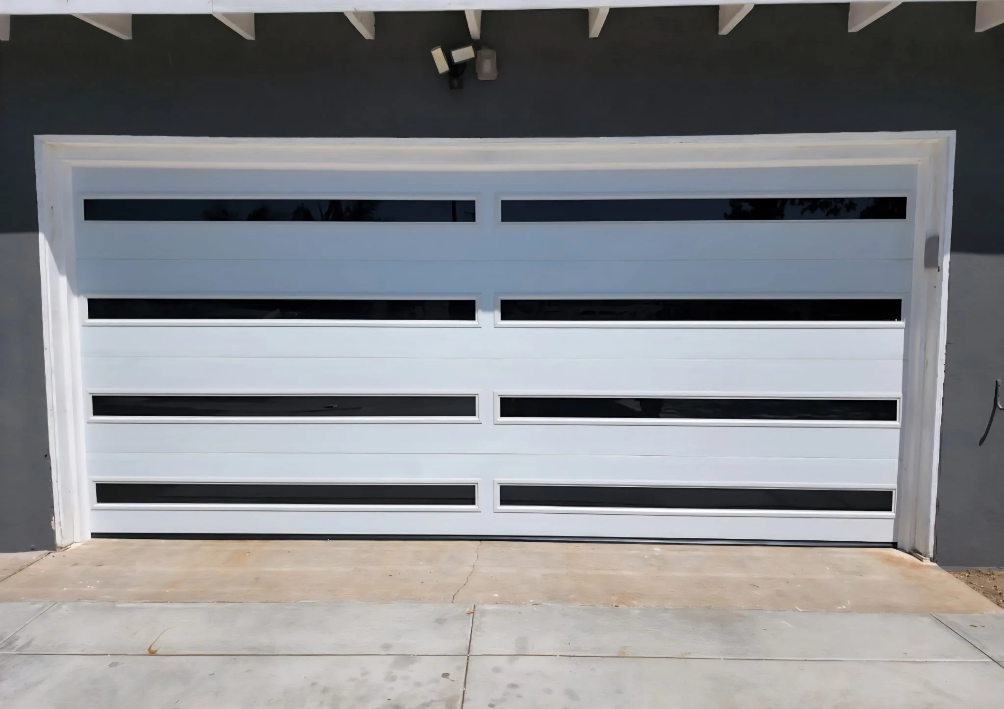 White garage door with horizontal windows, installed in a gray house with a concrete driveway.