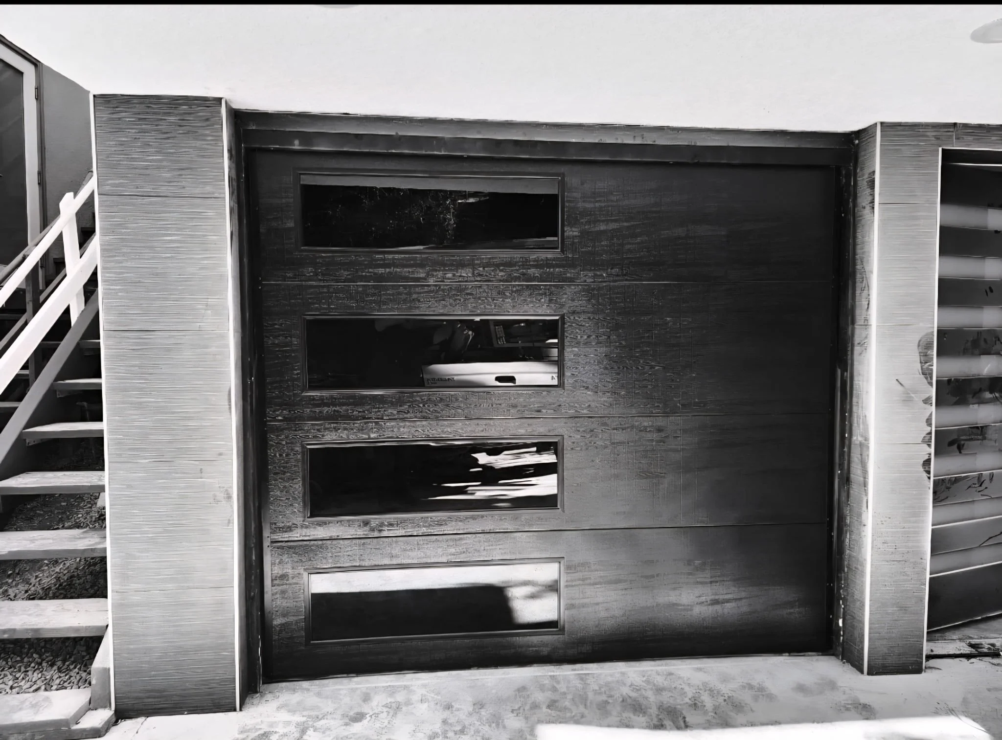 A modern garage door with horizontal rectangular windows, surrounded by wood-textured panels, and flanked by stairs on both sides.