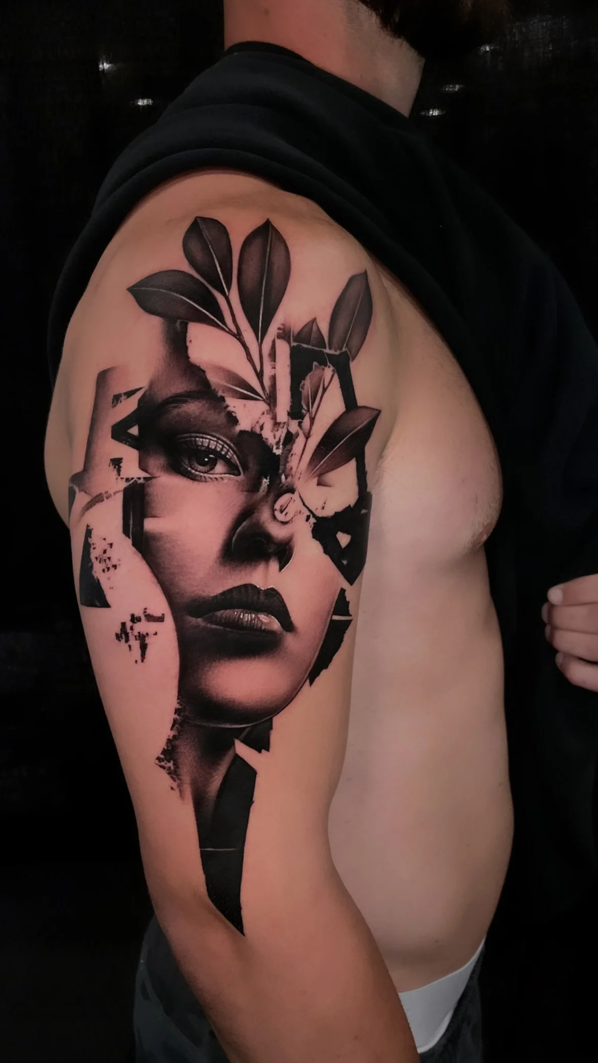 Tattoo of a woman's face with leaves and abstract design on upper arm.
