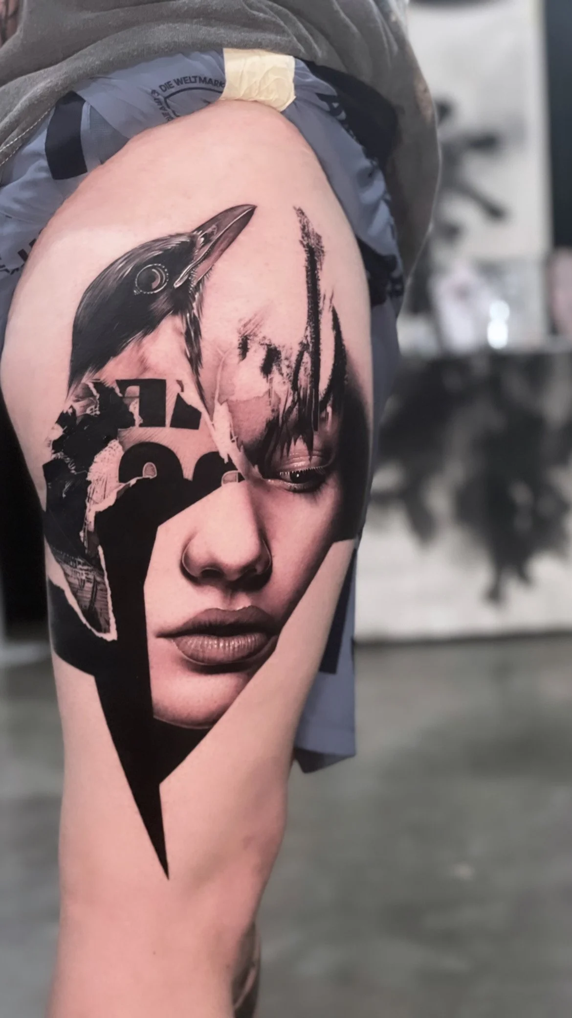 Tattoo of a woman's face with a bird's head on her forehead, combining photo realism and collage art styles.