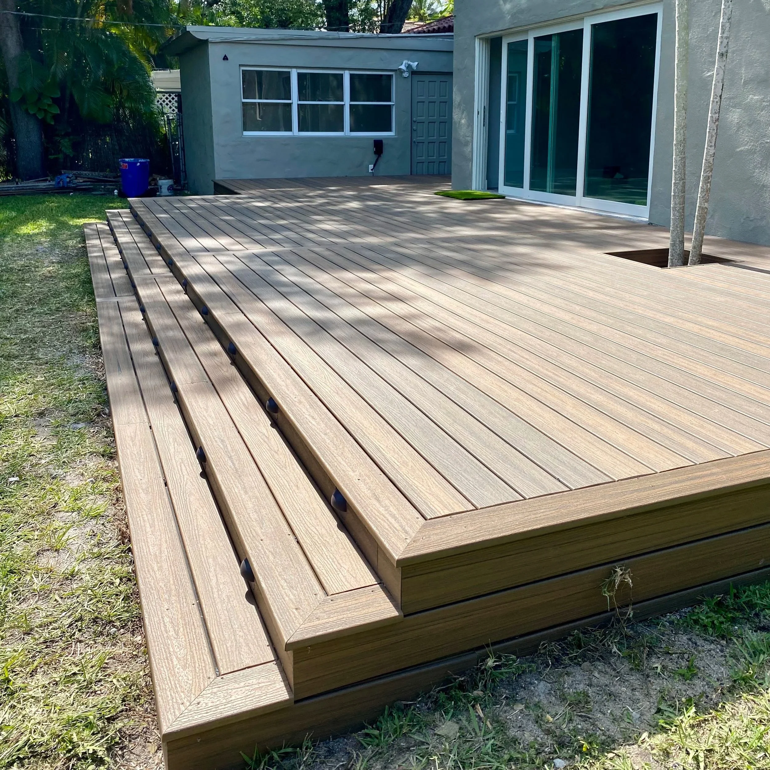 A newly built wooden deck attached to a house with sliding glass doors, with a small patch of grass and trees nearby.