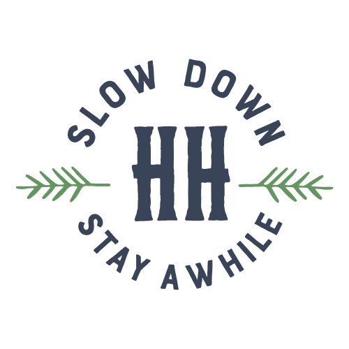 A circular logo with the text 'Slow Down Stay Awhile' surrounding the initials 'HH' in the center, with green decorative leaves on each side.