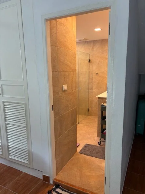 A doorway leads into a bathroom with beige tiled walls and a white sink area in the background.