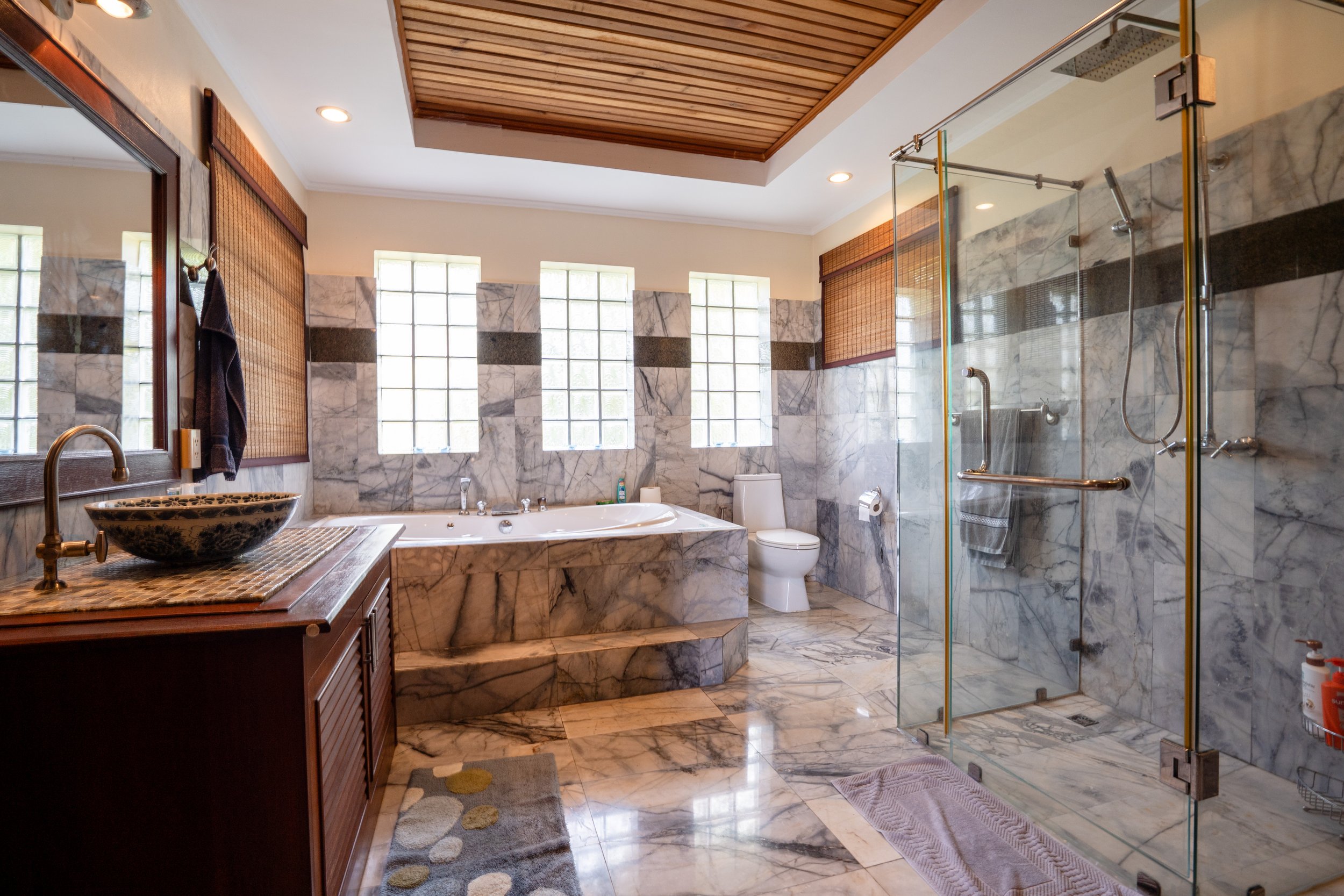 Marble bathroom with vanity, vessel sink, bathtub, toilet, and glass-enclosed shower with robes and towels