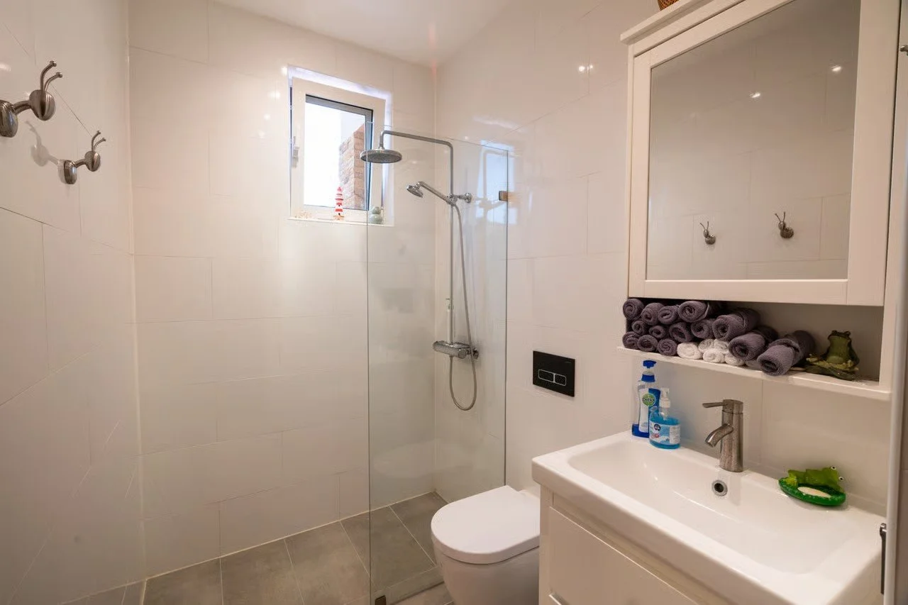Modern bathroom with walk-in shower, wall mirror cabinet, towels, soap, and hand sanitizer.