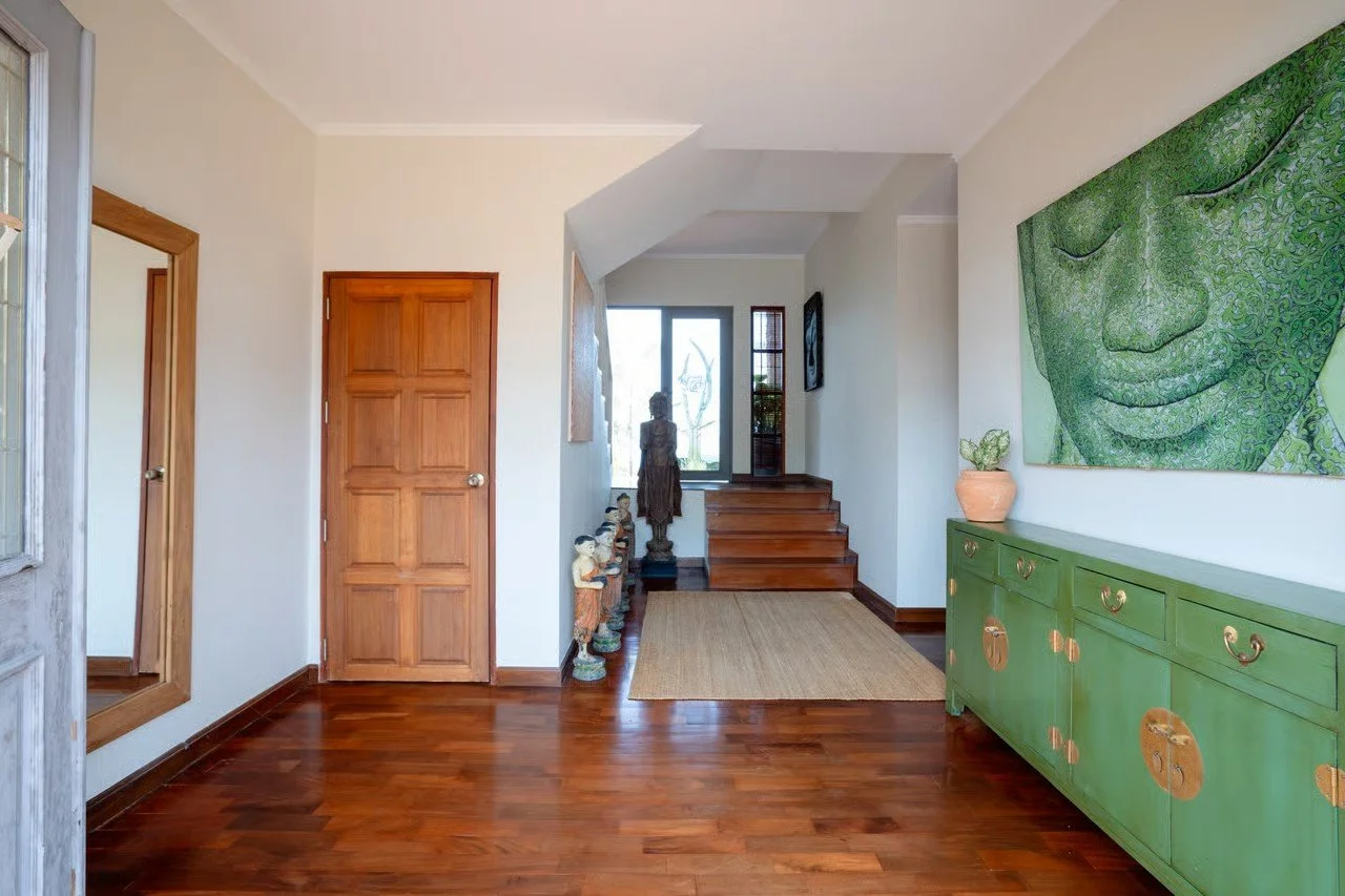 Entryway with wooden floor, green sideboard, large wall art of a face, wooden staircase, and Asian-style decor