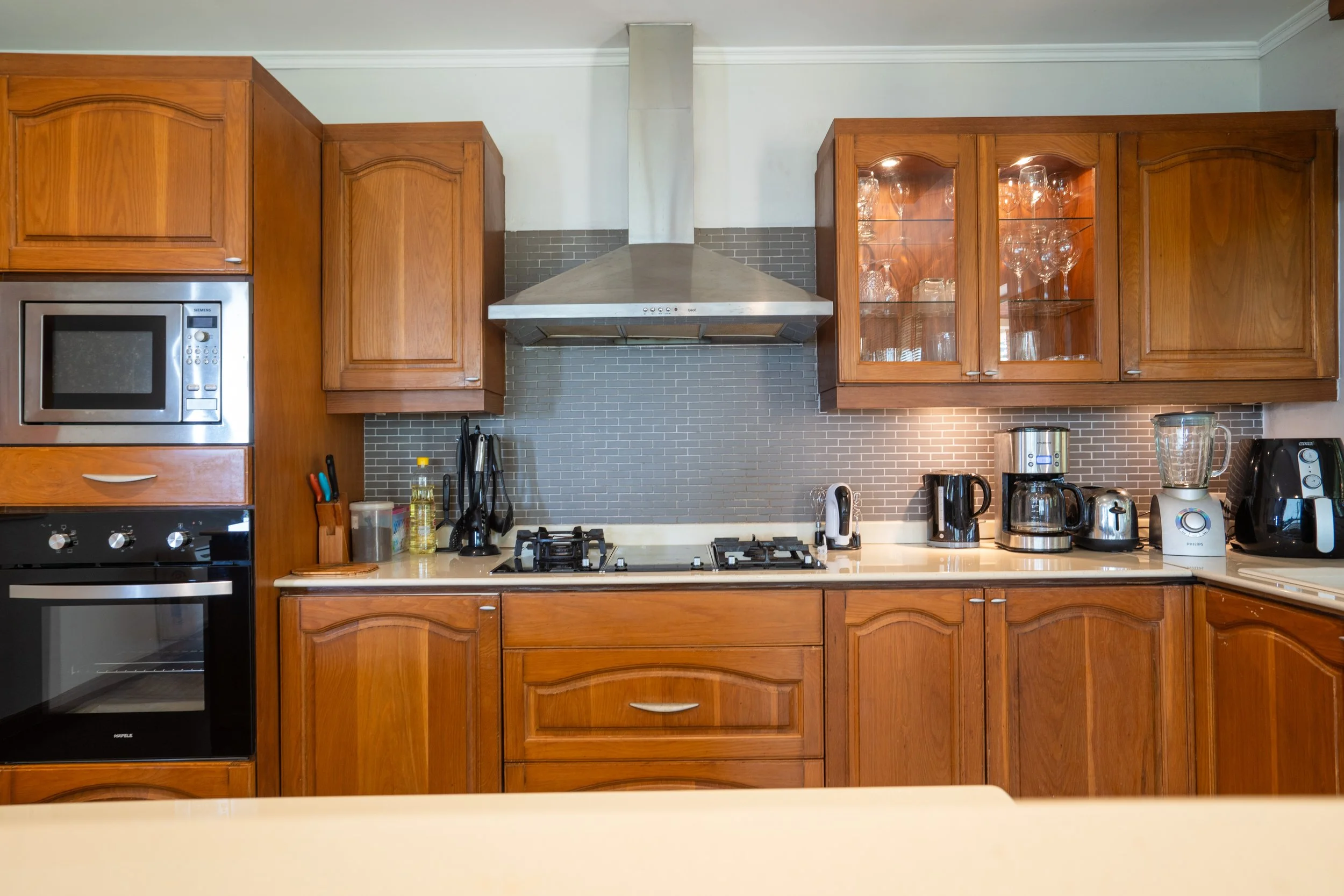 Kitchen with wooden cabinets, stainless steel microwave and oven, gas stove, range hood, and various small appliances on the countertop, including a blender, coffee maker, and toaster.