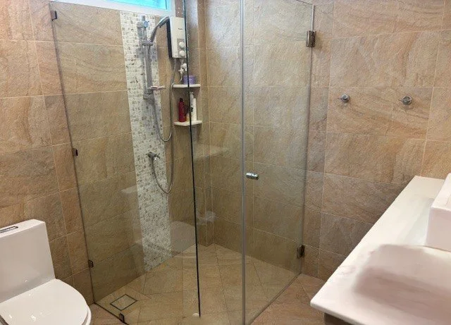 A modern bathroom with a glass-enclosed walk-in shower, a white toilet, and a white vanity with a sink.