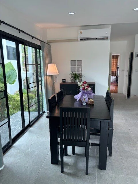 Dining room with black wooden table and chairs, vase of flowers, floor lamp, large sliding glass doors, and modern decor.