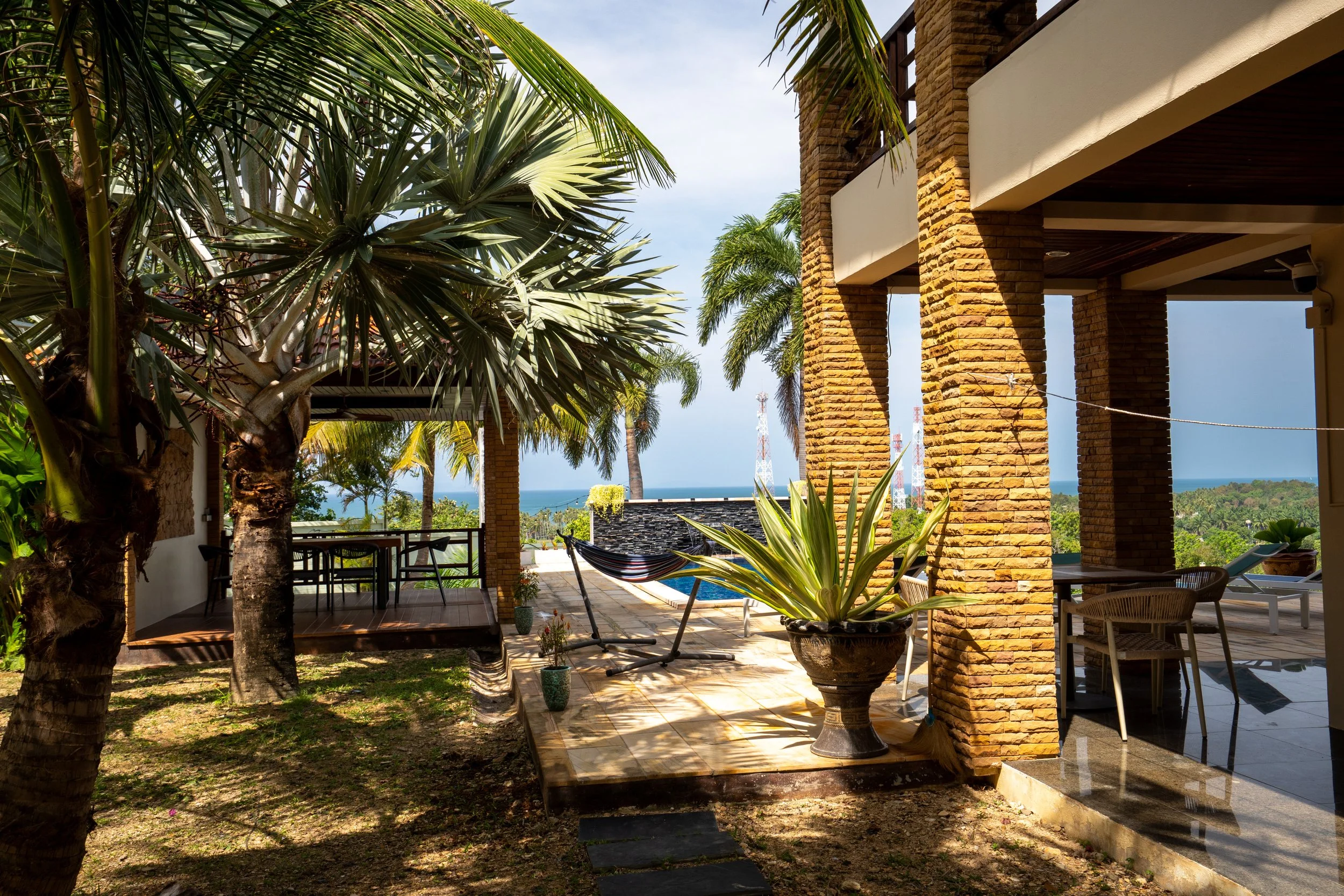Outdoor patio with tropical plants, a hammock, a swimming pool, and ocean view in the background.
