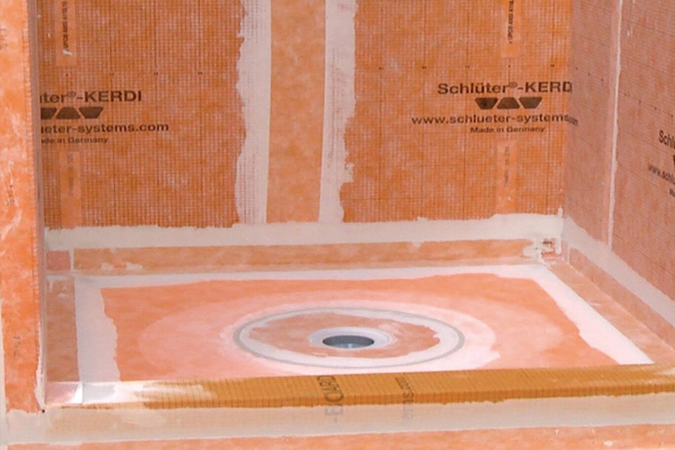 Interior of a bathroom with unfinished brick walls and a circular drain in the floor, with insulation material marked 'Schlüter-KERD' on the walls.