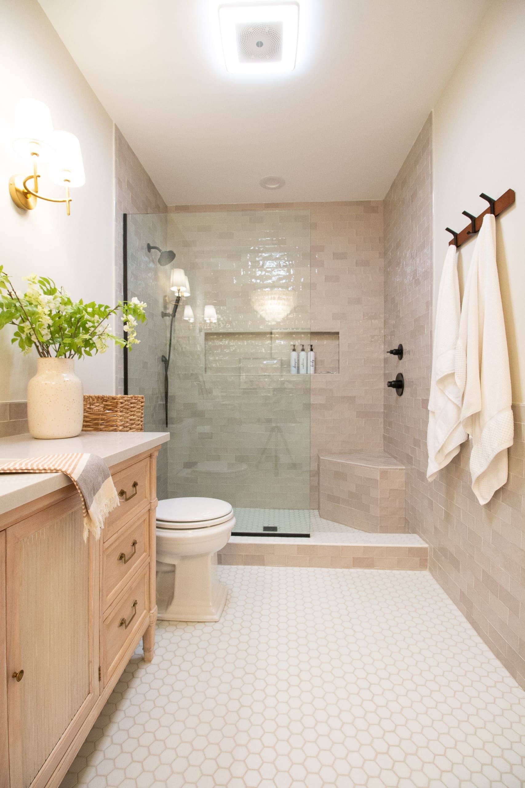A bathroom with a beige vanity, a potted plant, a toilet, a glass-shower enclosure, and white towels hanging on a rack.