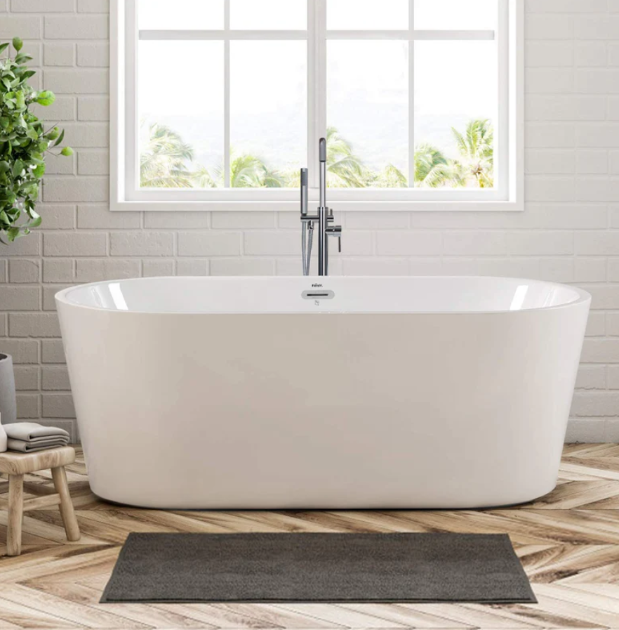 A modern freestanding white bathtub in a bright bathroom with a large window, wood floor, and a gray rug.