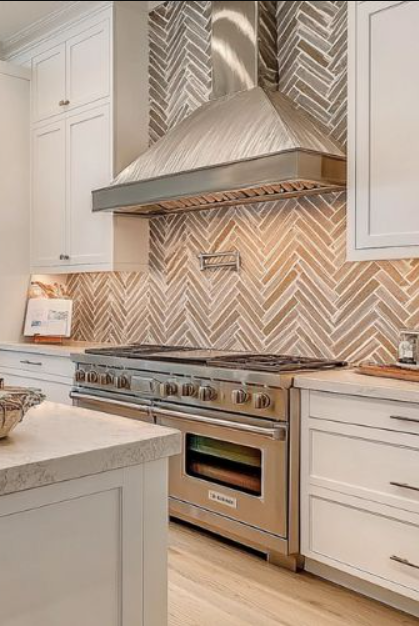 Modern kitchen with white cabinets, a stainless steel oven and range hood, and a chevron-patterned tile backsplash.