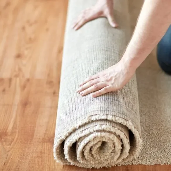 Person unrolling a beige carpet on a wooden floor.