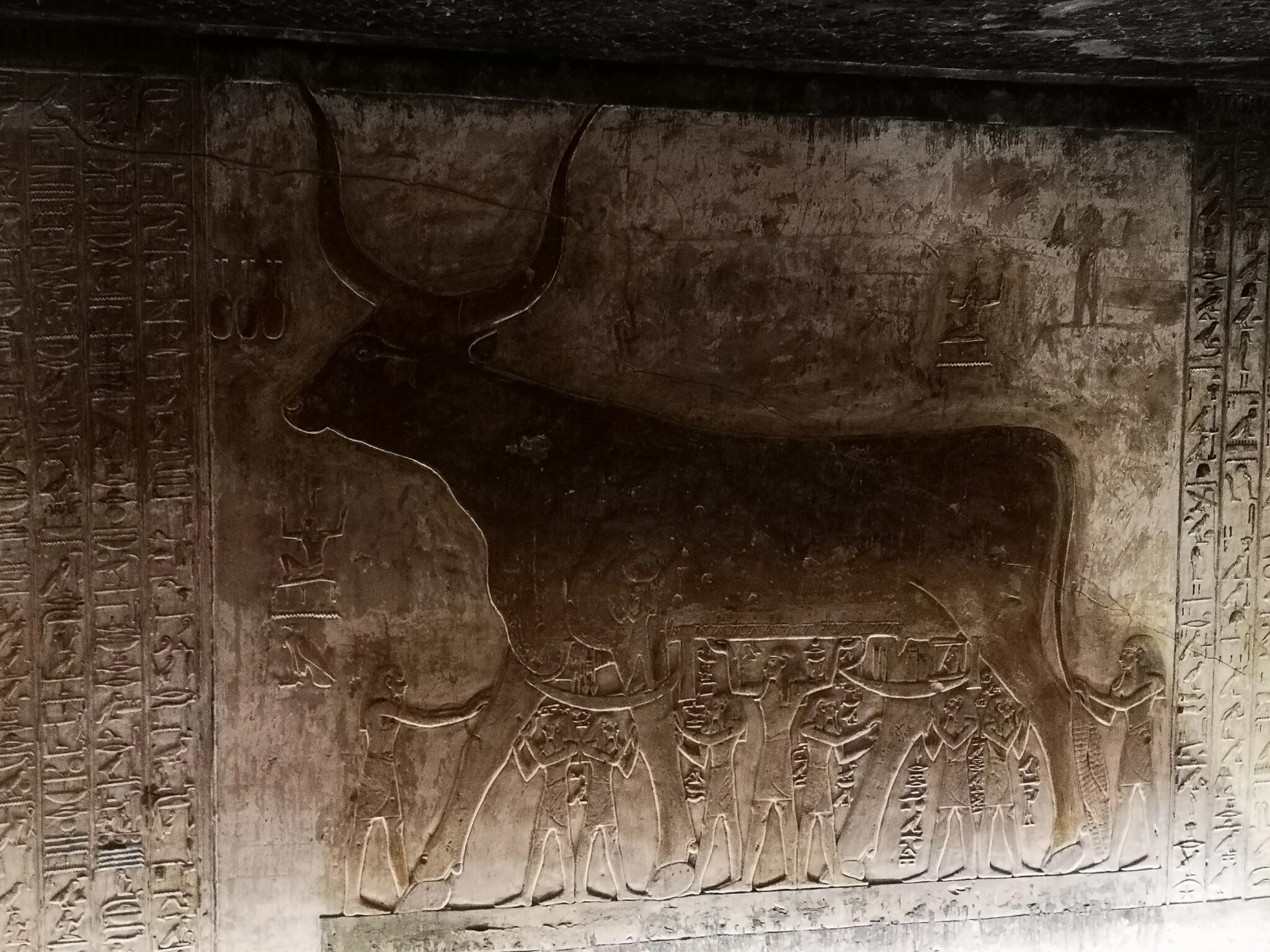 Wall relief of the Heavenly Cow with horns, eight human figures beneath the cow, surrounded by columns of hieroglyphs in the tomb of Seti I.