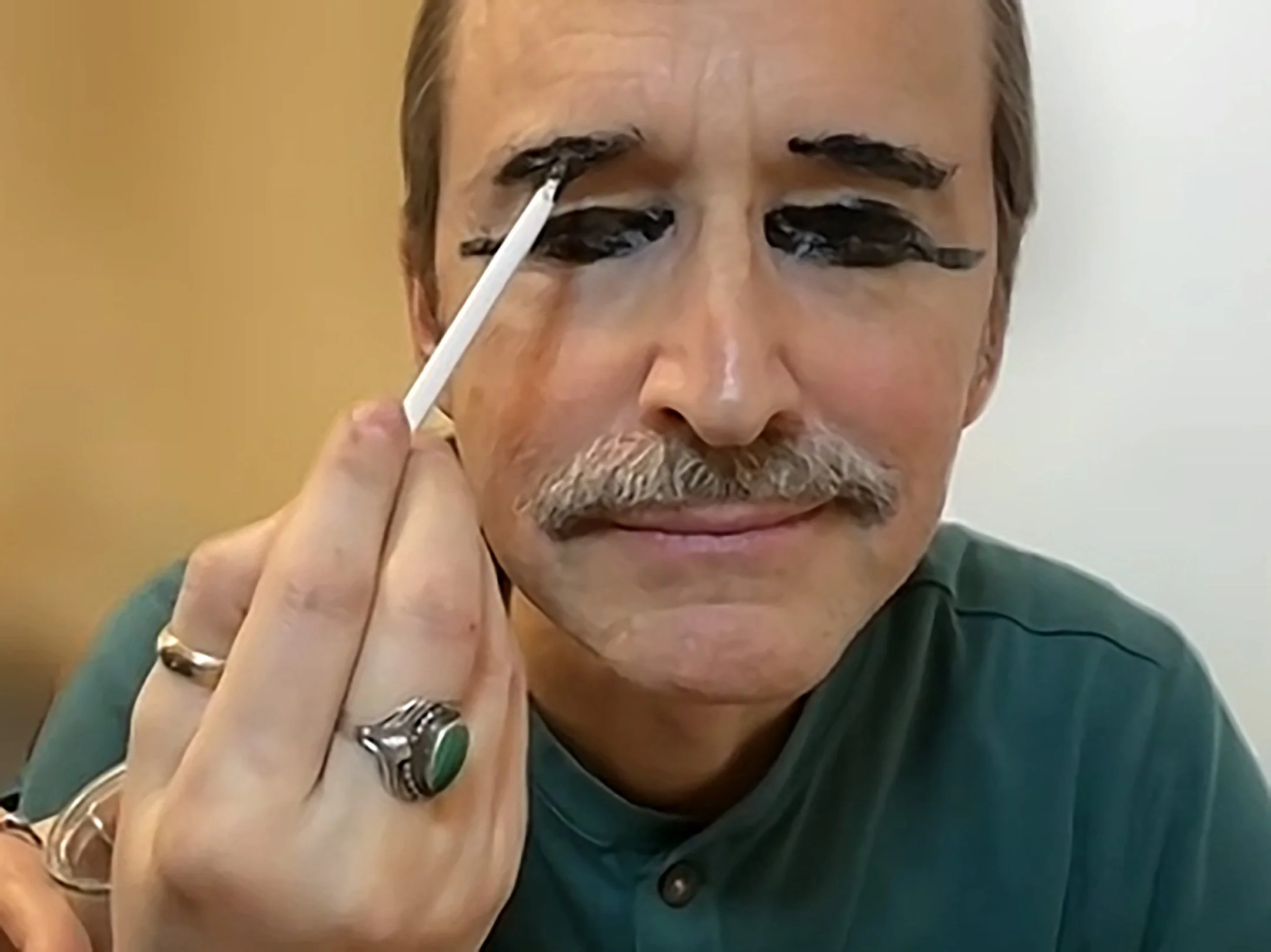 Close‑up of a face as a white brush applies thick black kohl around the eye.